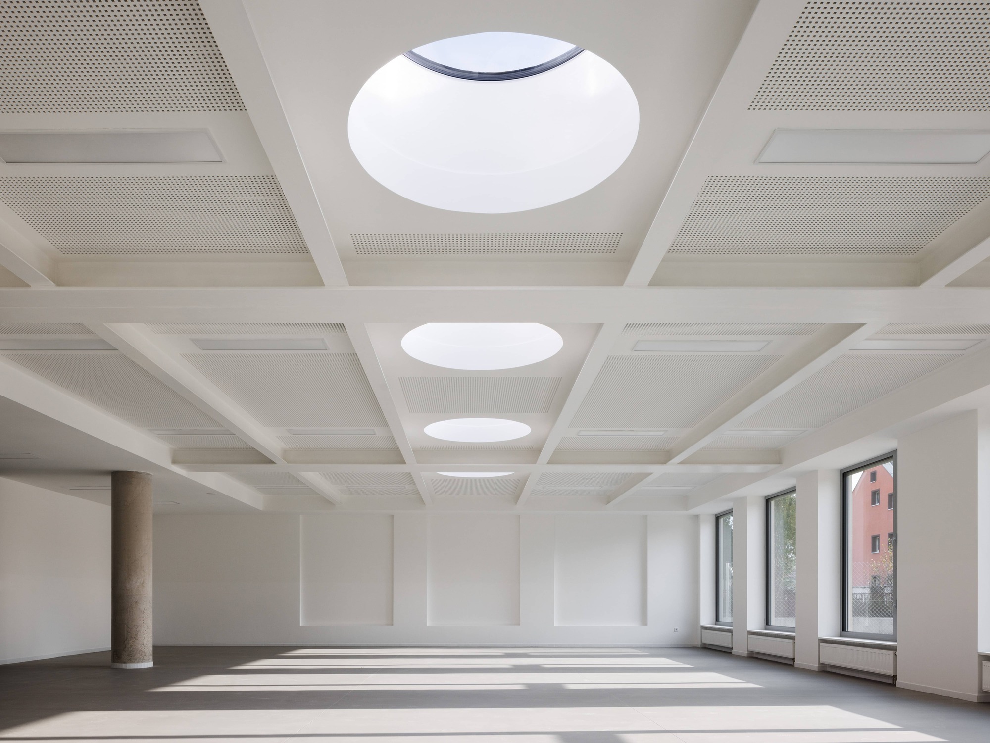 Interior hall with coffered ceiling featuring circular skylights and sunlight casting patterns across the floor