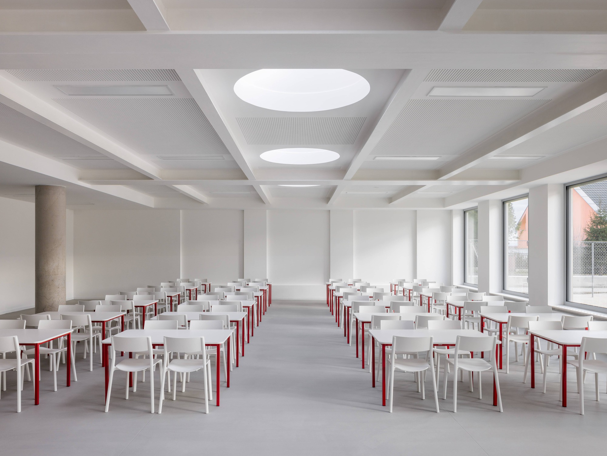Dining hall with white and red chairs arranged in rows beneath circular ceiling apertures