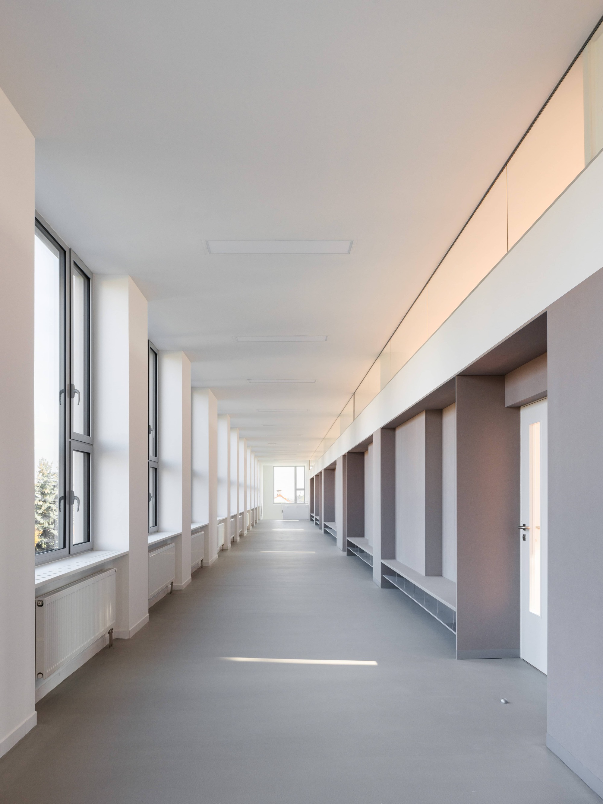 Long corridor with rhythmic window openings on the left and a series of recessed doorways and built-in benches on the right