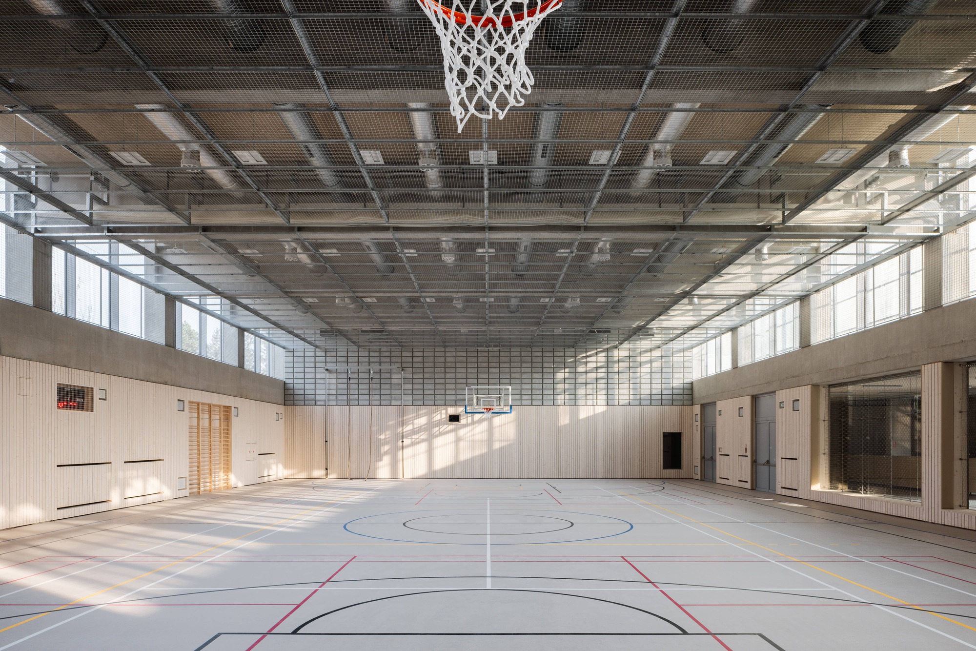 Sports hall with exposed metal grid ceiling and timber wall panels along the perimeter