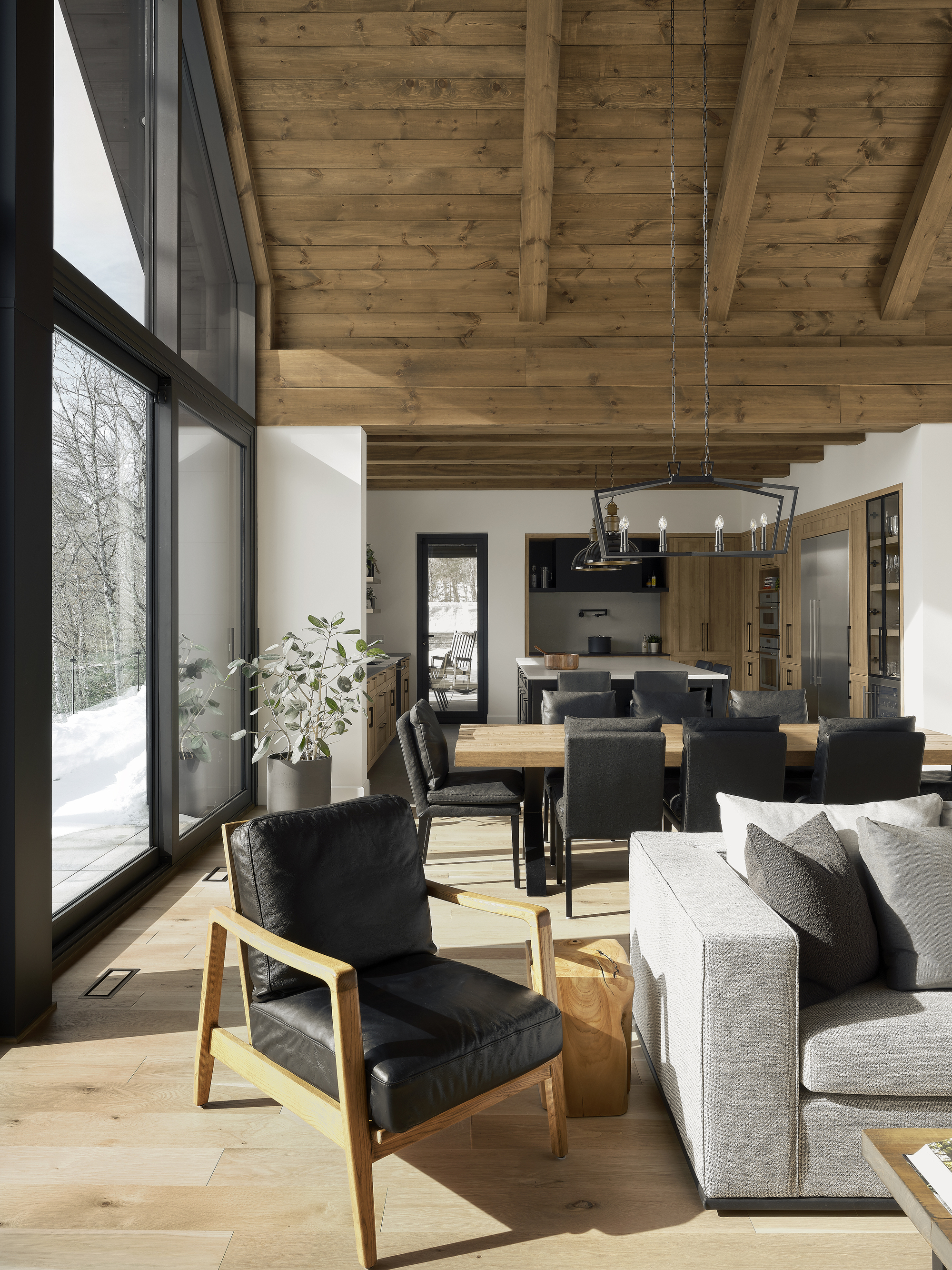 Open living space with exposed timber ceiling beams and tall glazing overlooking snowy forest