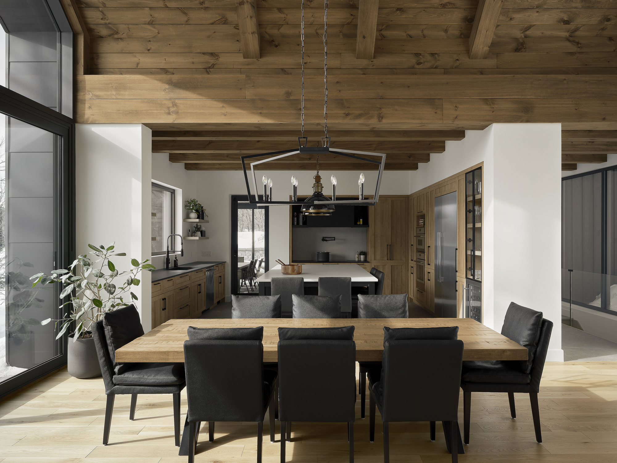 Open dining area with exposed timber ceiling beams and black metal pendant light above wood table