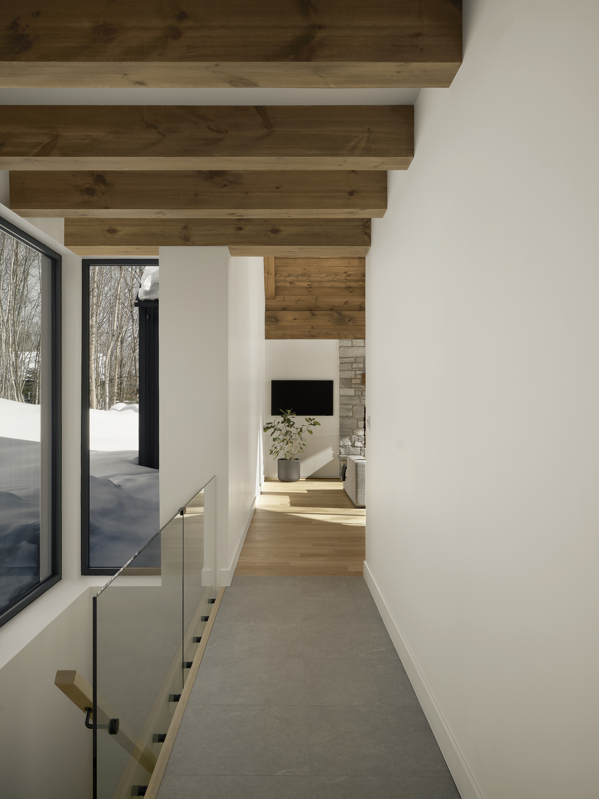 White corridor with exposed timber ceiling beams and glass balustrade overlooking snowy exterior