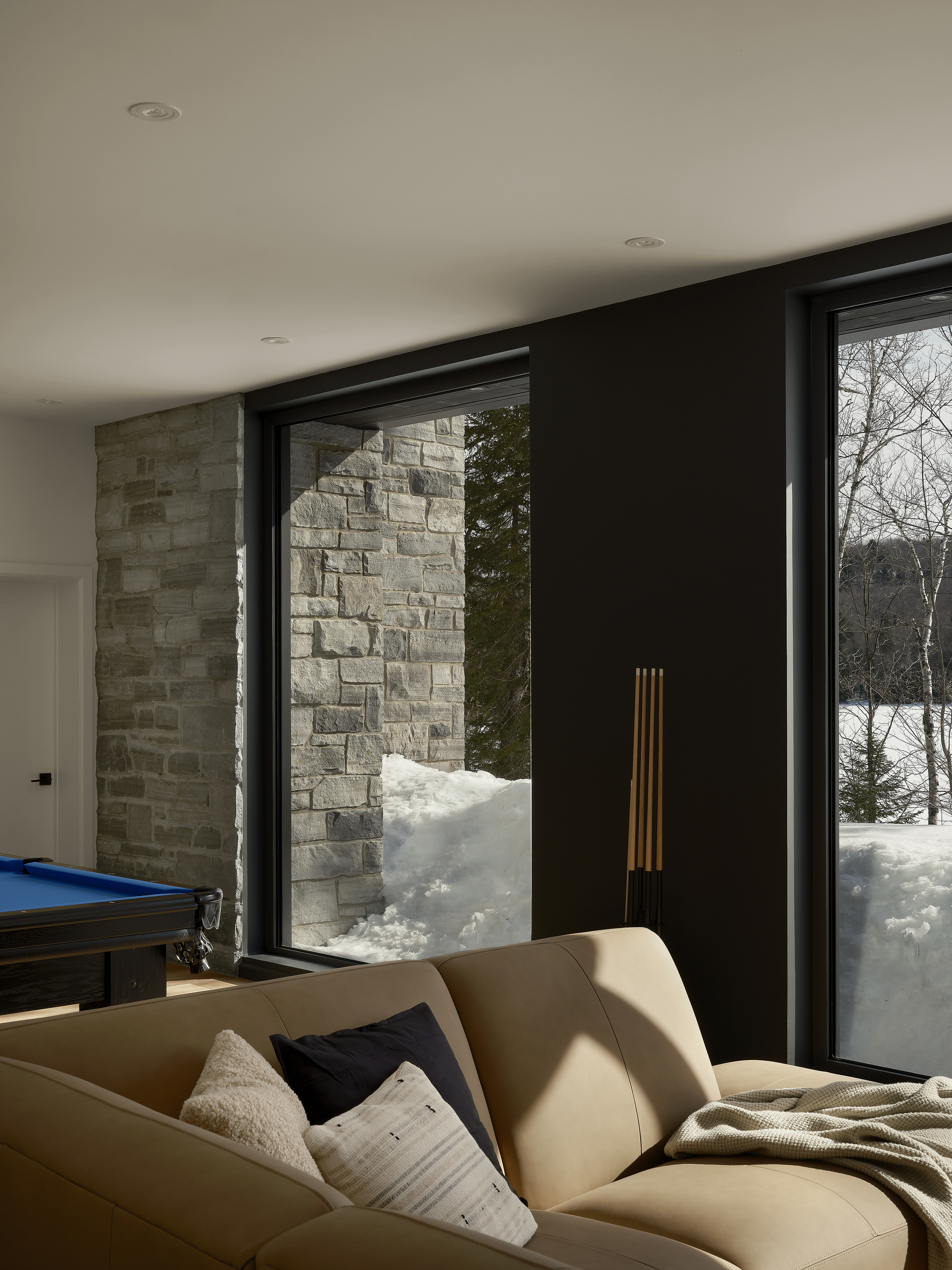 Corner lounge with black-framed glazing beside textured stone wall in winter sunlight