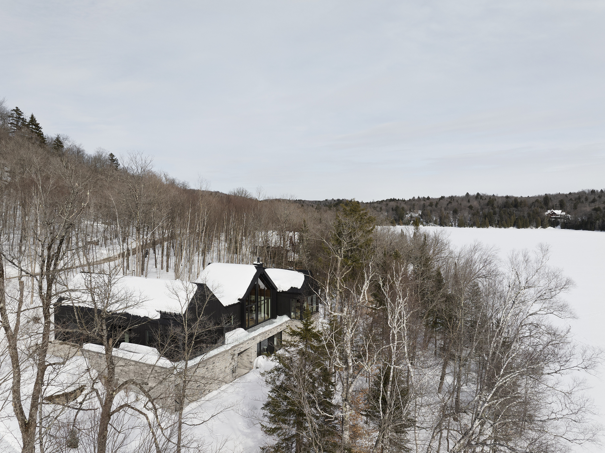 Distant view of the stone and timber residence on a hillside among bare and evergreen trees