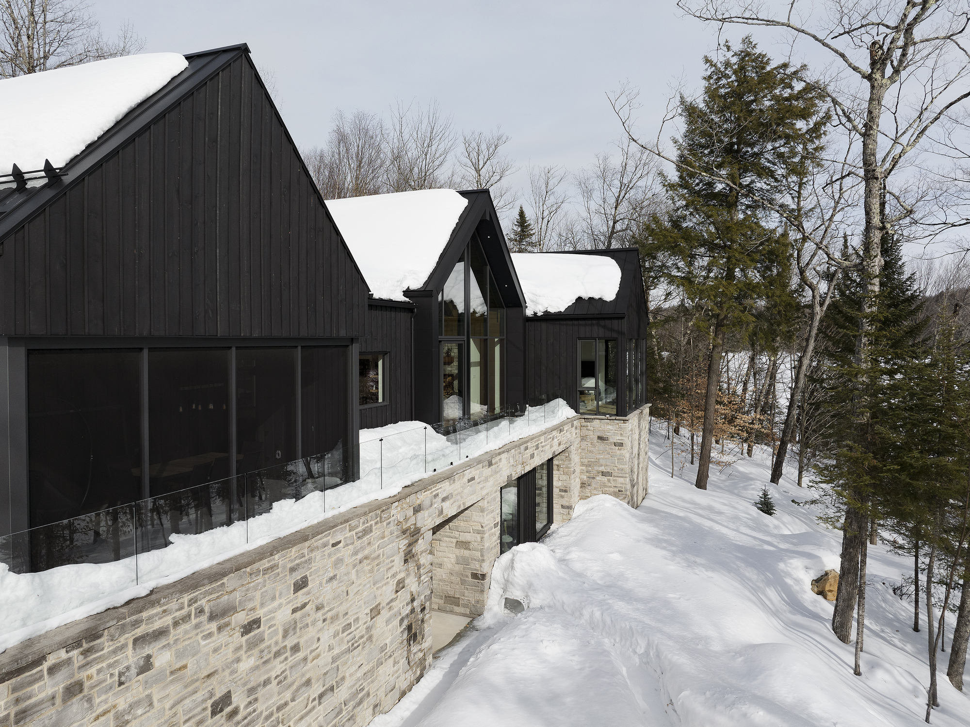 Exterior view of the black timber cladding and stone base terrace with snow on the sloped site