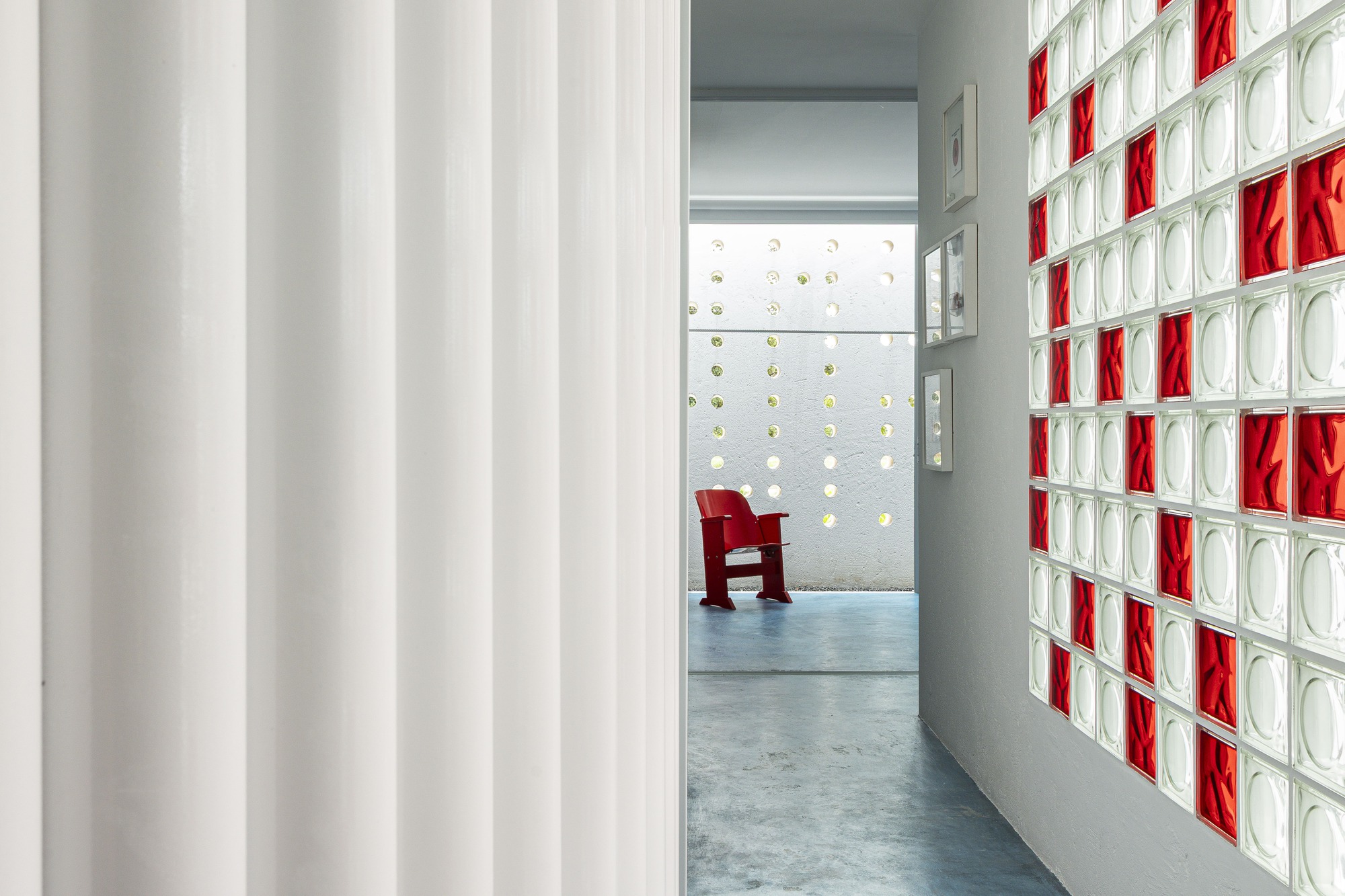 Corridor with white fabric curtain and red and clear glass block wall with a red chair visible beyond