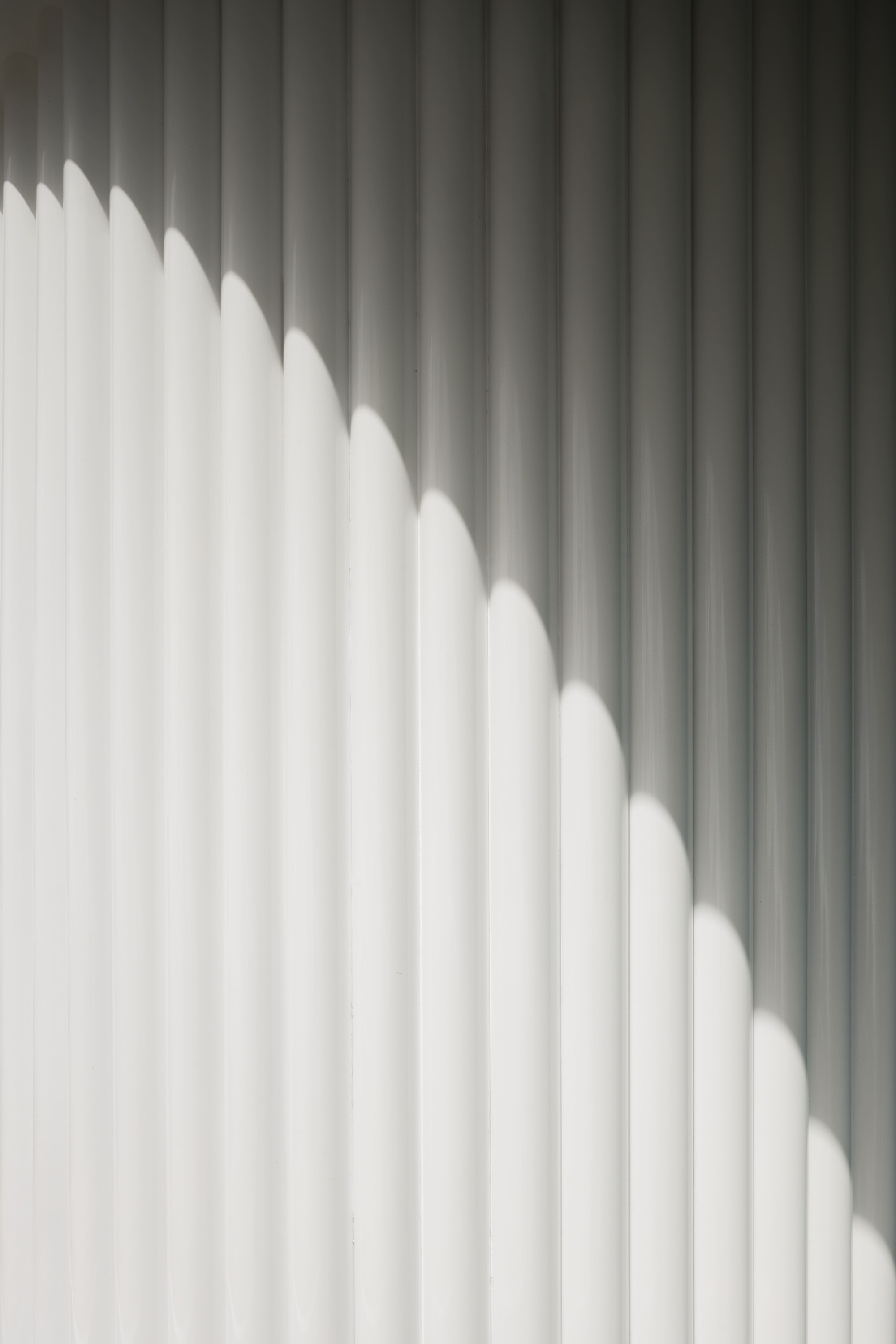 Diagonal shadow pattern cast across white vertical slat wall in natural daylight