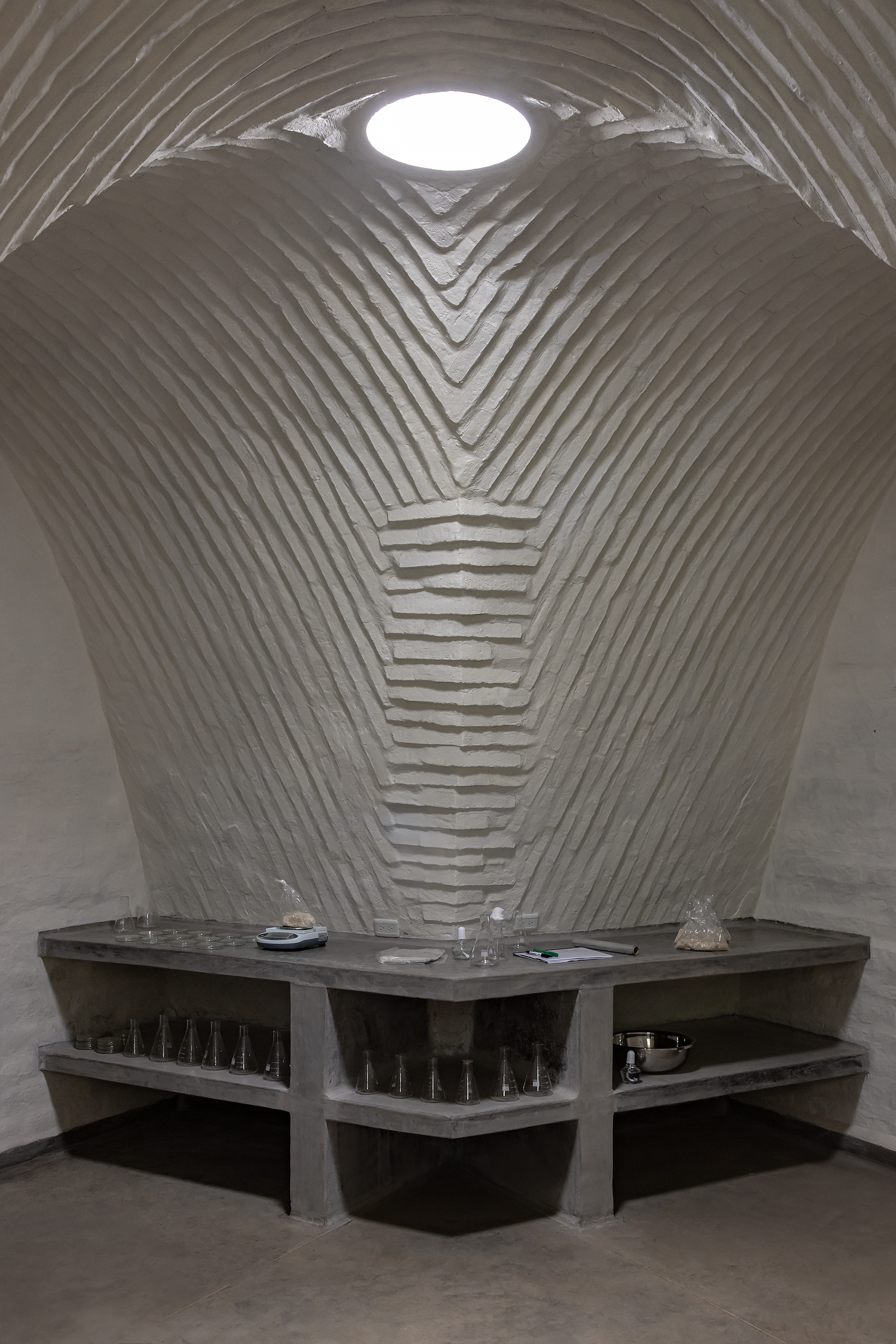 Vaulted space with circular skylight above stepped concrete counters and glassware