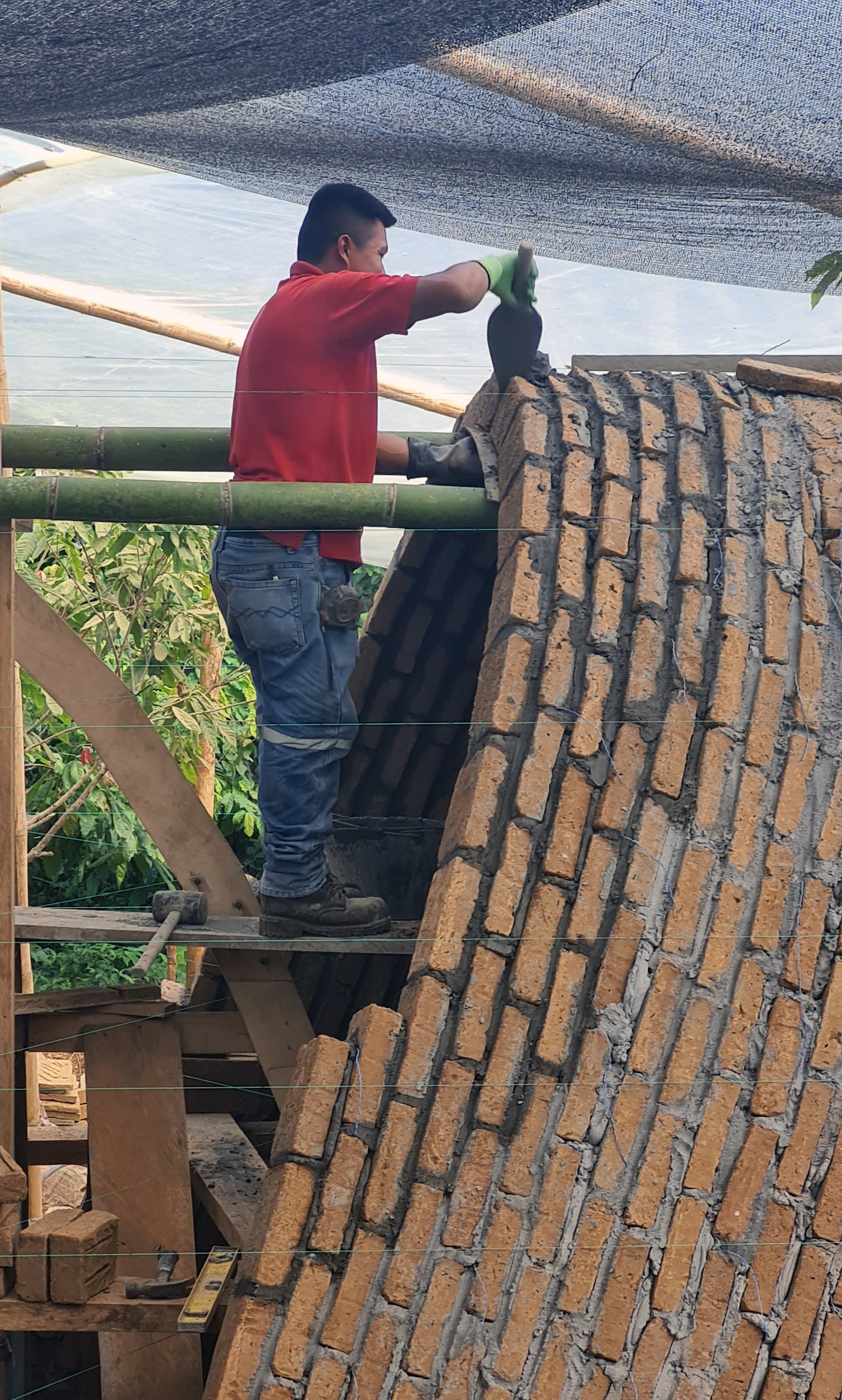 Worker applying plaster to a curved brick roof supported by bamboo scaffolding