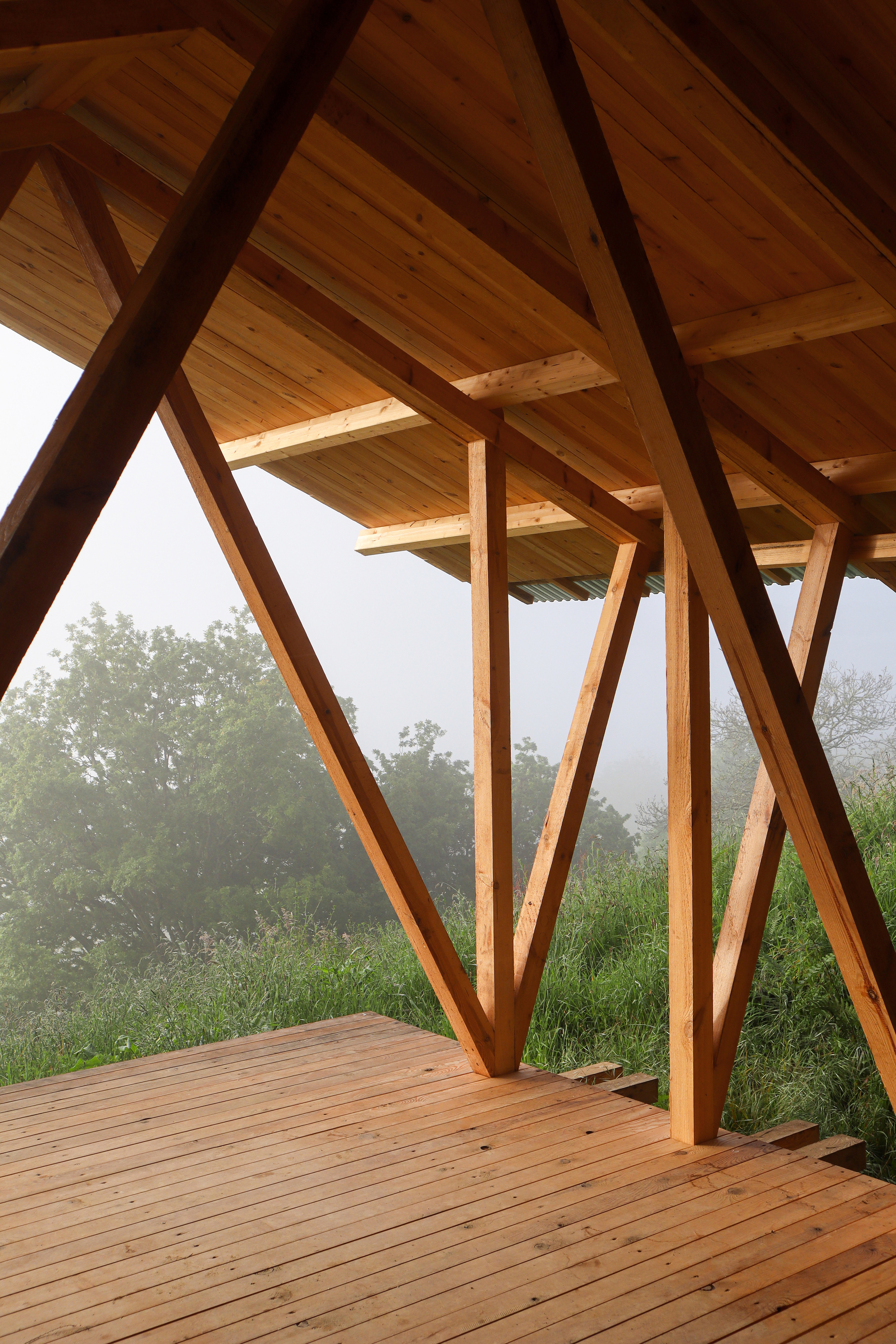 Interior view of the angled timber columns supporting wood plank ceiling with valley landscape visible through the opening