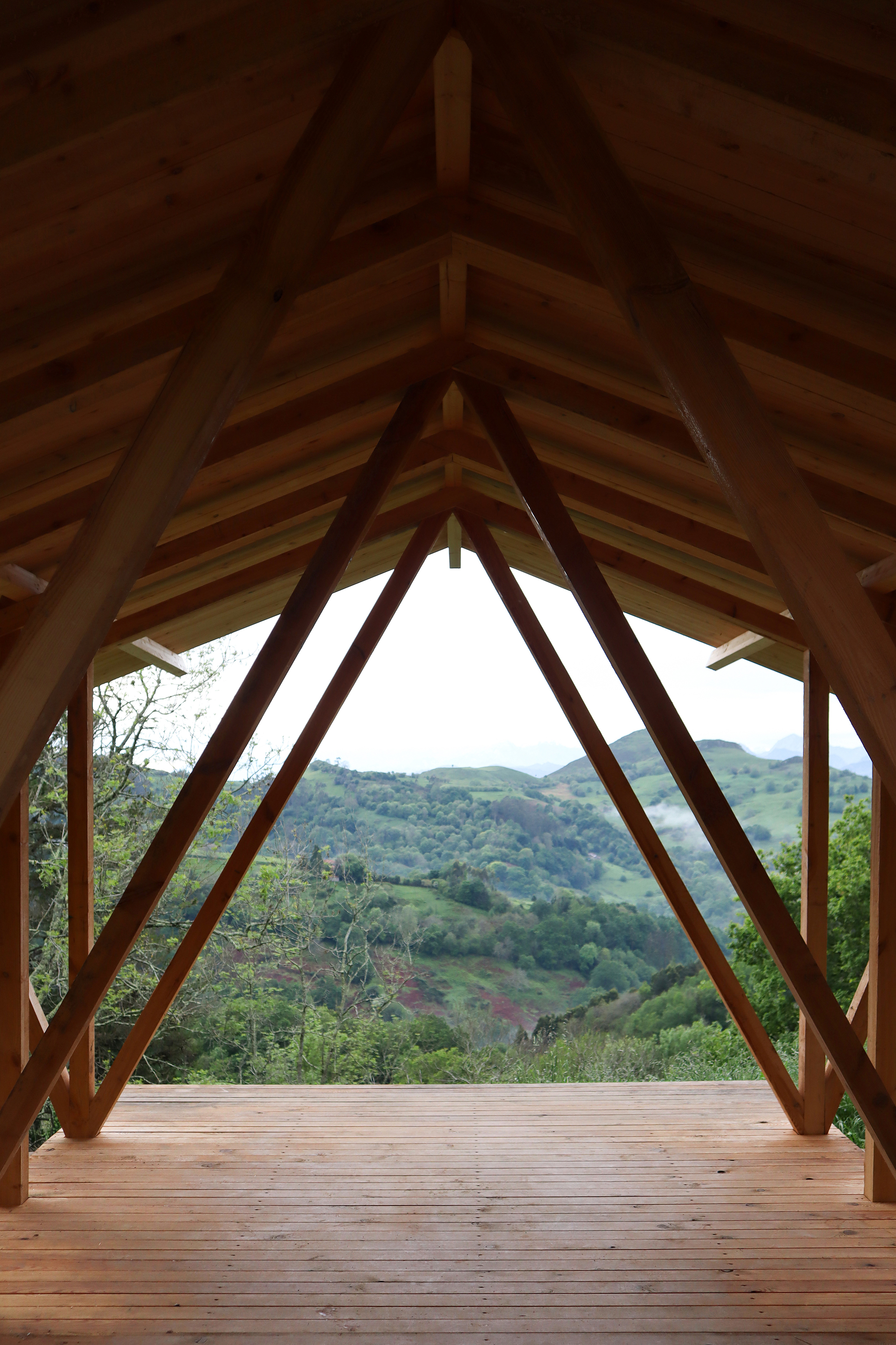 Interior view through the timber frame structure overlooking rolling green hills in the distance