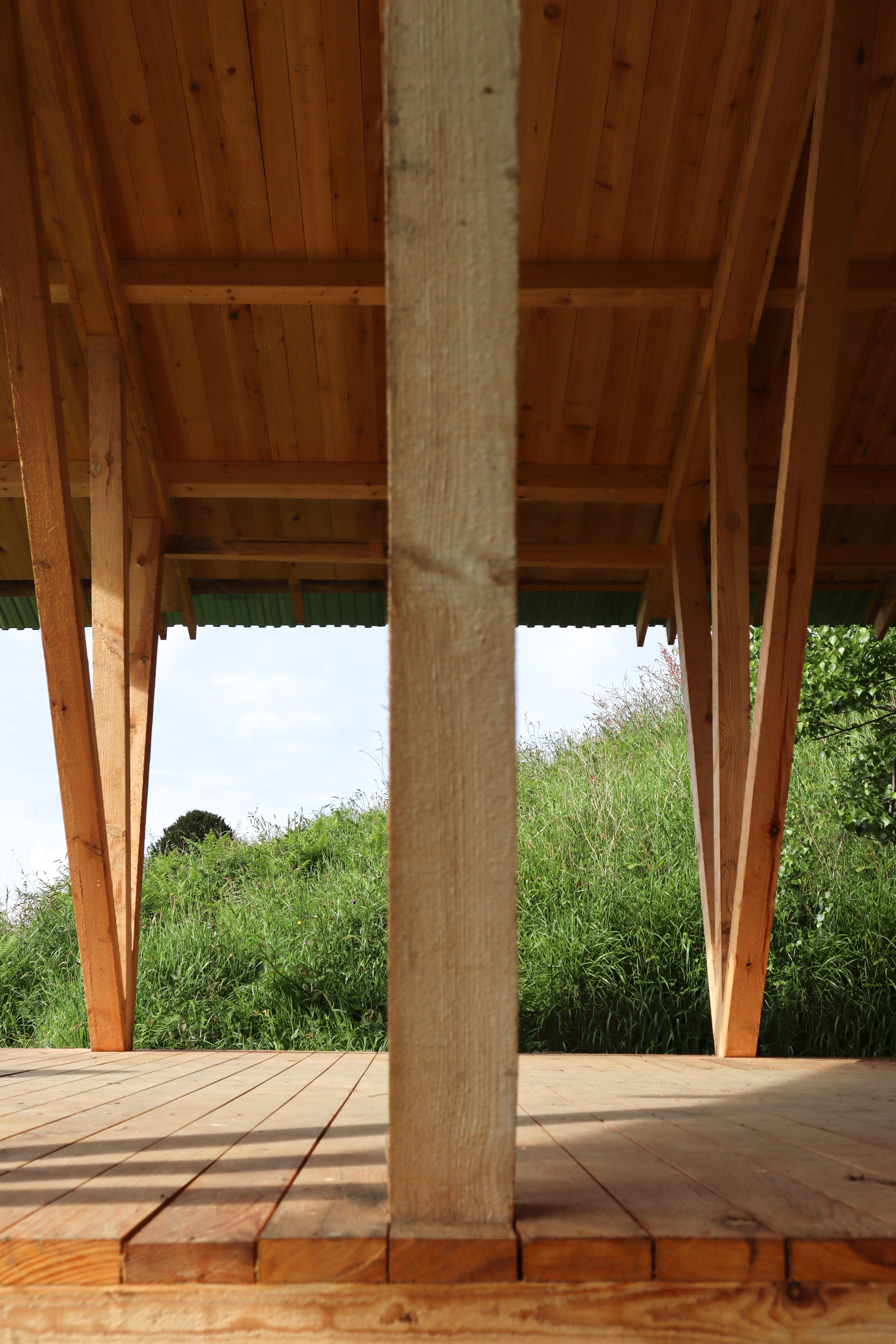 Wrapped column detail on timber deck beneath exposed rafter ceiling framing grassy slope beyond