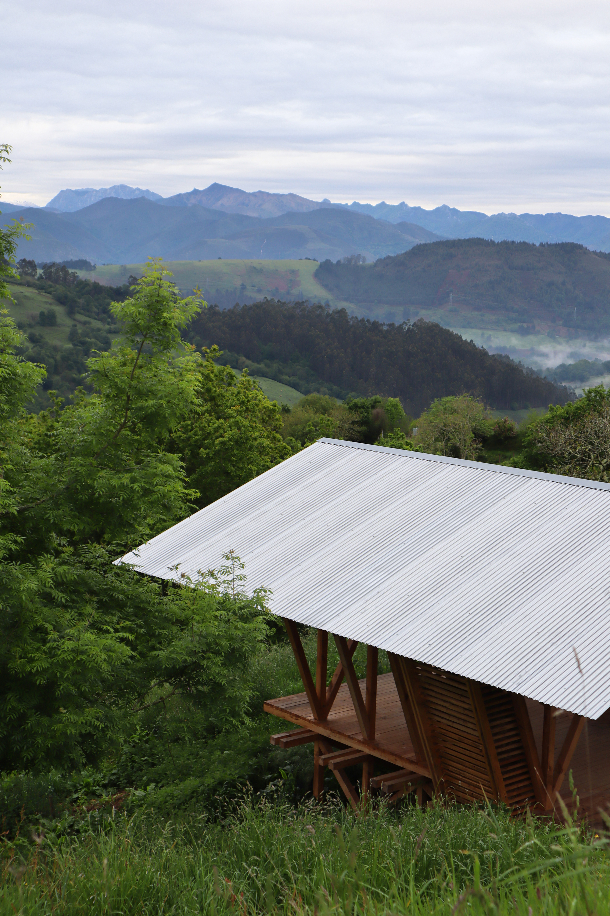 Open-sided structure with corrugated roof and timber frame overlooking layered mountain ridges with morning mist