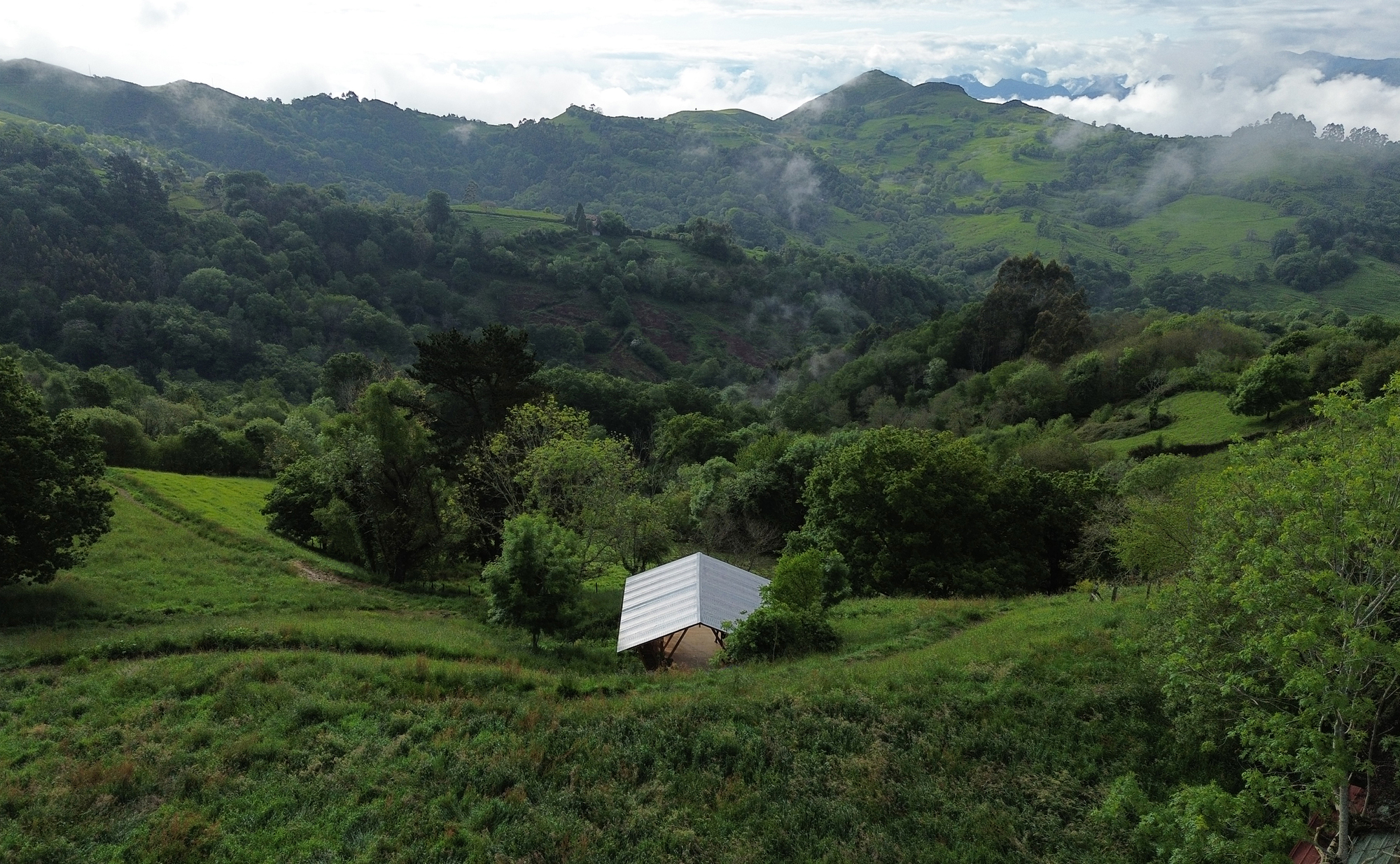 Small pavilion with white corrugated roof nestled in a valley among rolling green hills