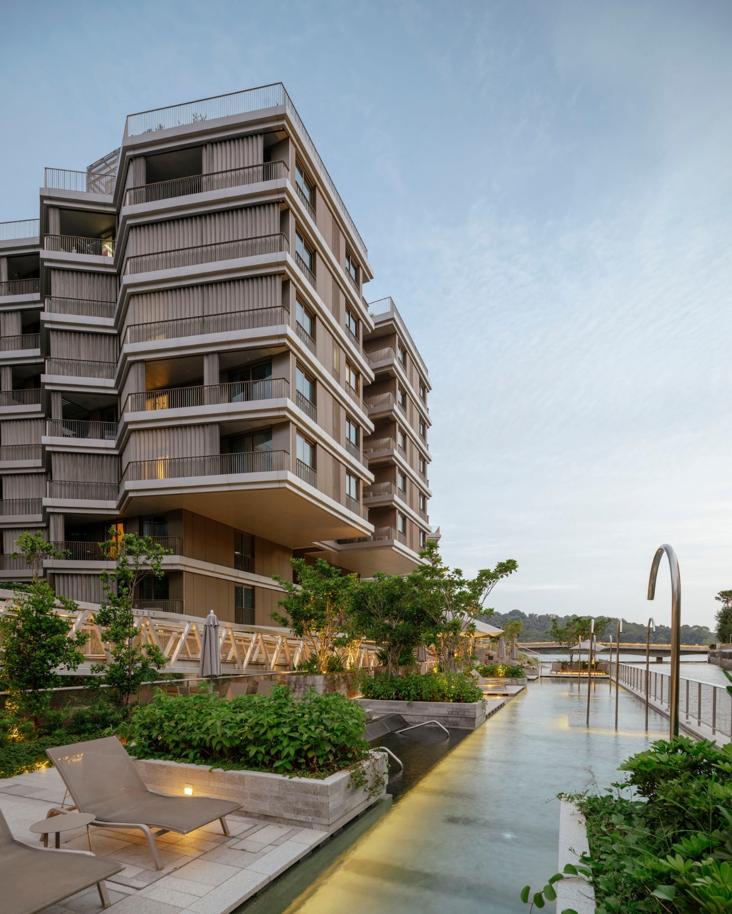 Rooftop pool deck with planted beds and residential towers rising above at twilight