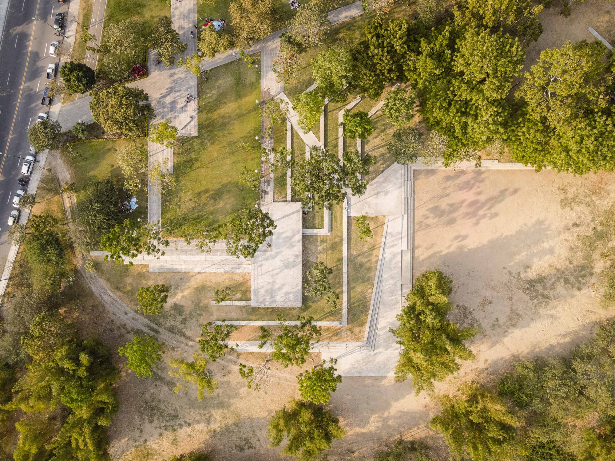 Drone view of a concrete pavilion with folded roof planes set among trees and lawn areas
