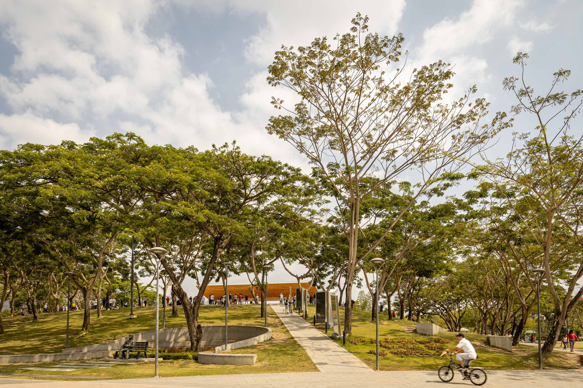Park pathways leading to a distant pavilion with a cyclist passing and circular water feature