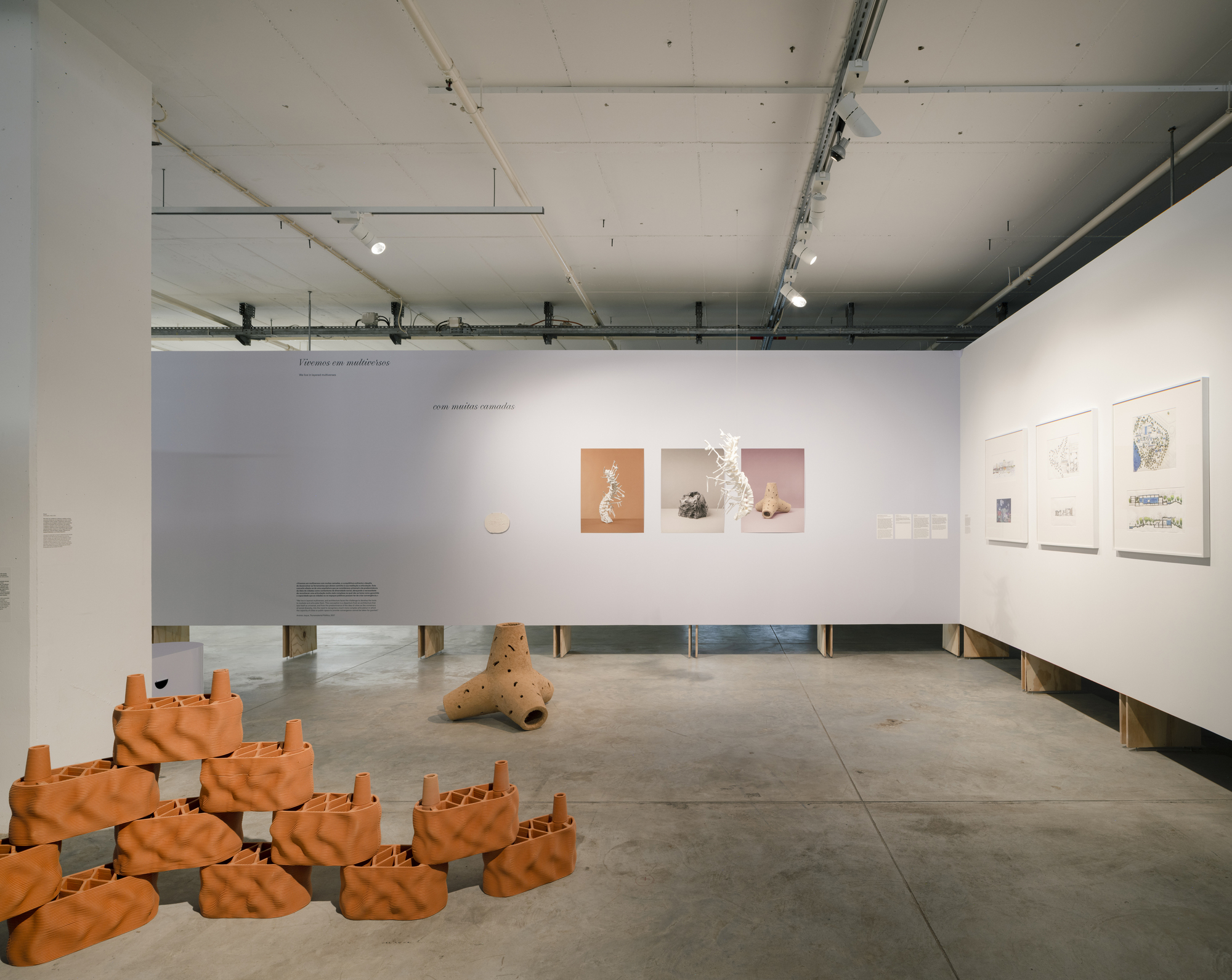 Gallery view of terracotta sculptural objects arranged on floor beside long plywood bench and white wall