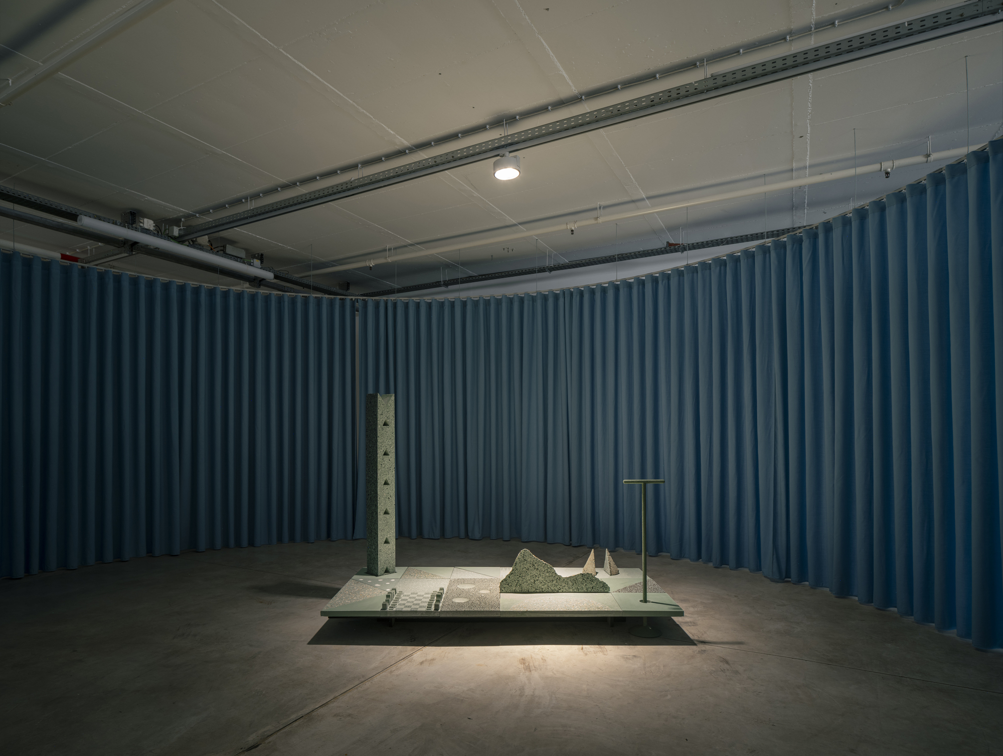 Enclosed gallery alcove with deep blue curtain walls surrounding a centered sculptural installation on platform
