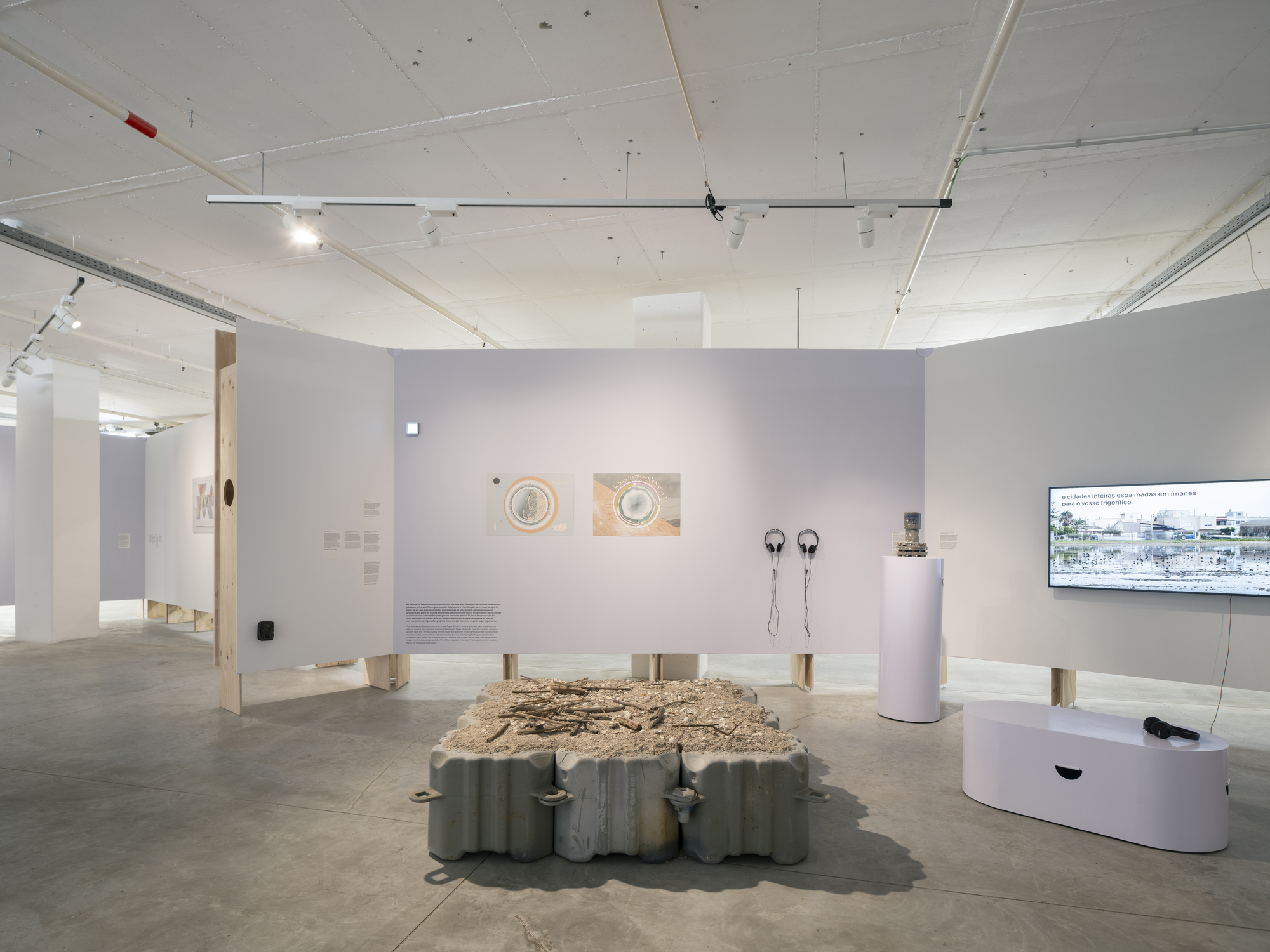 Gallery interior with white walls displaying artworks and a central table with textured surface under track lighting