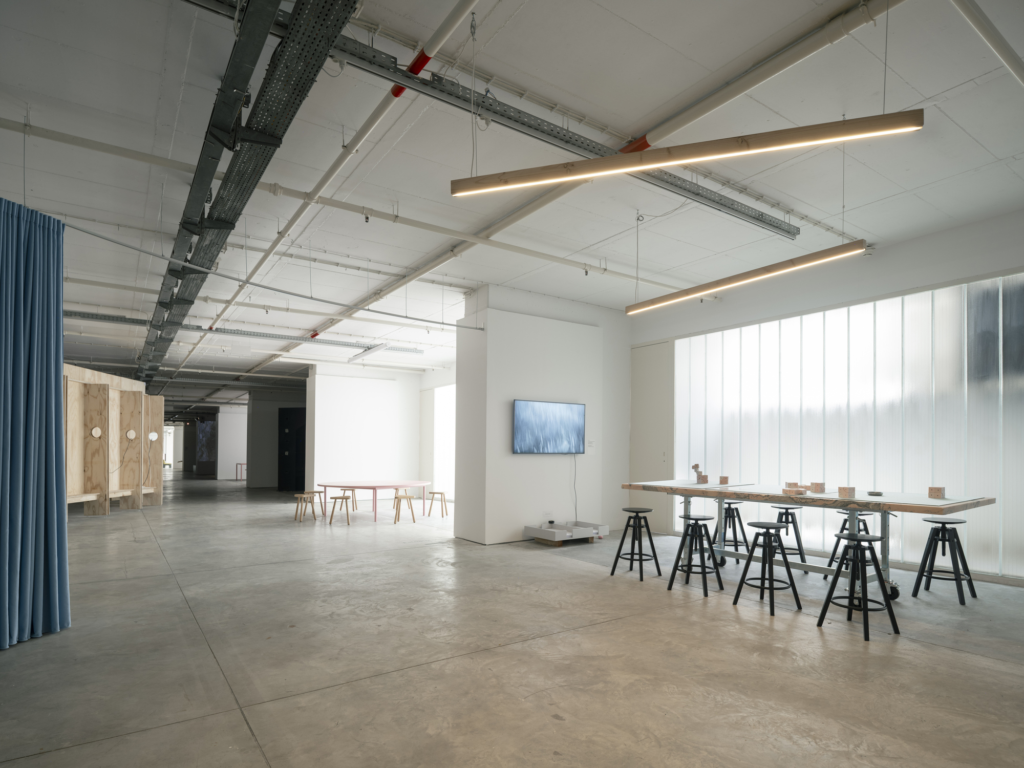 Open gallery space with work table on trestles and vertical white panel wall under linear pendant lights