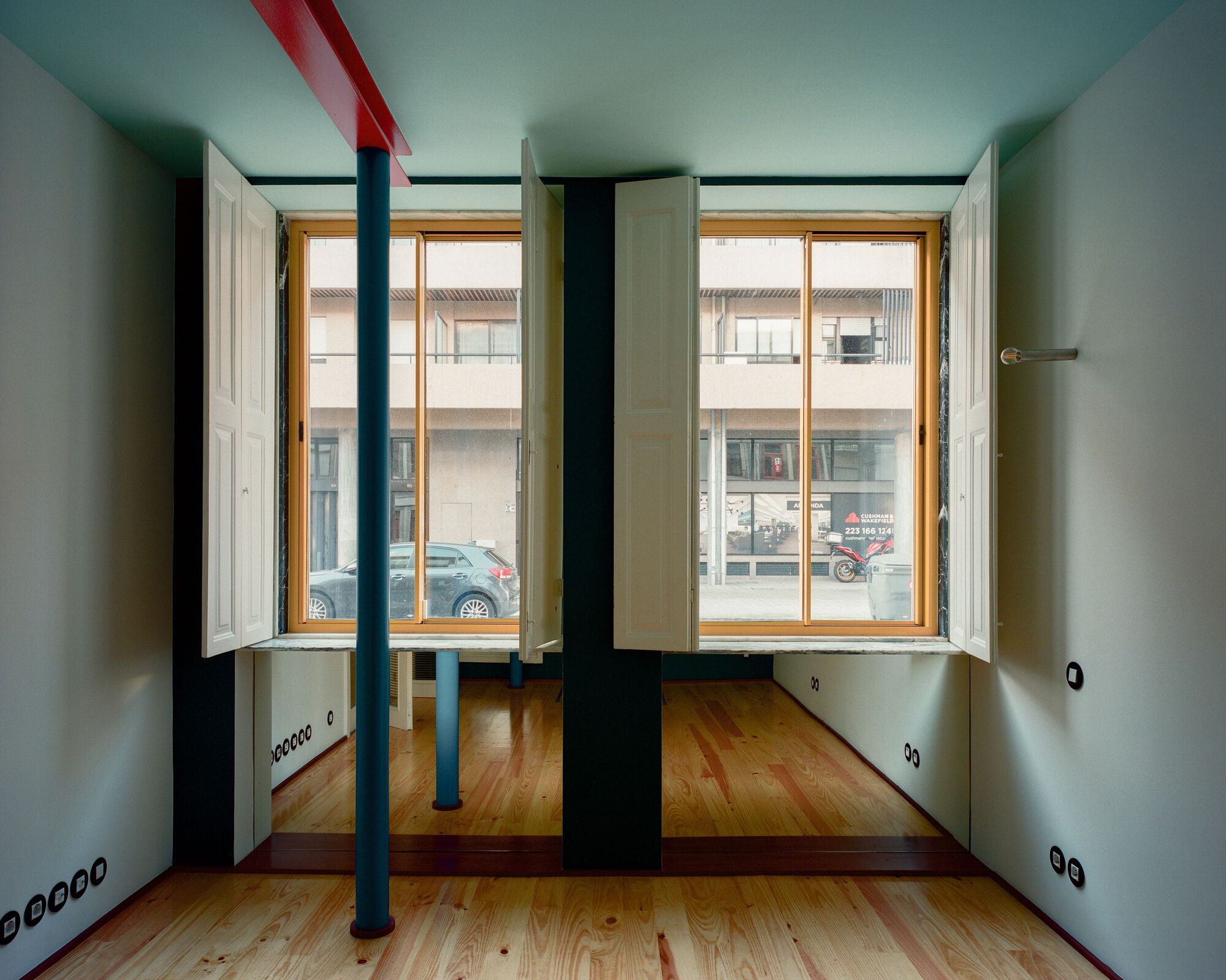 Interior room with pine flooring, painted steel columns, and timber-framed windows overlooking the street