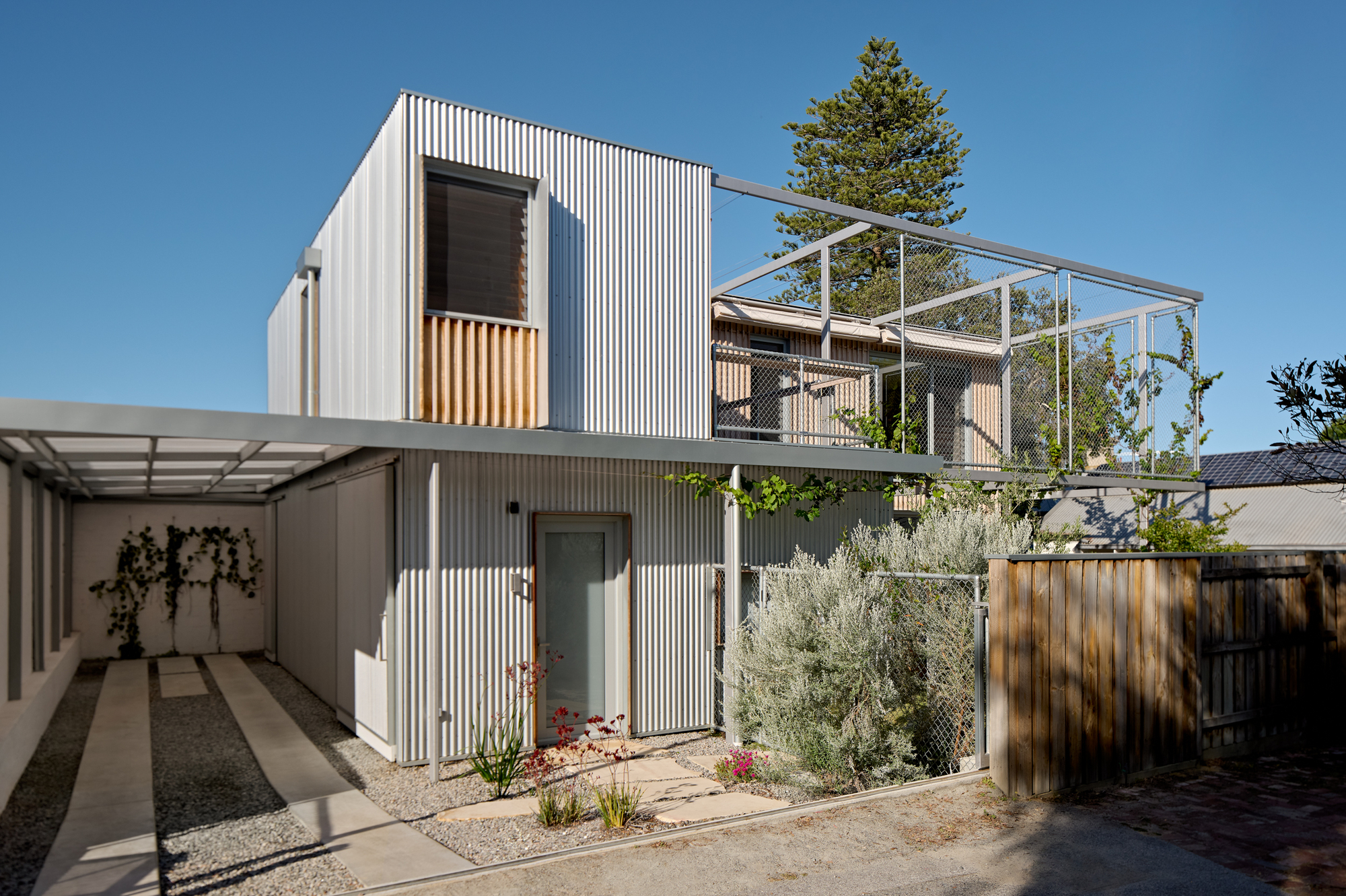 Two-storey corrugated metal facade with timber accents and upper-level steel mesh balcony enclosure