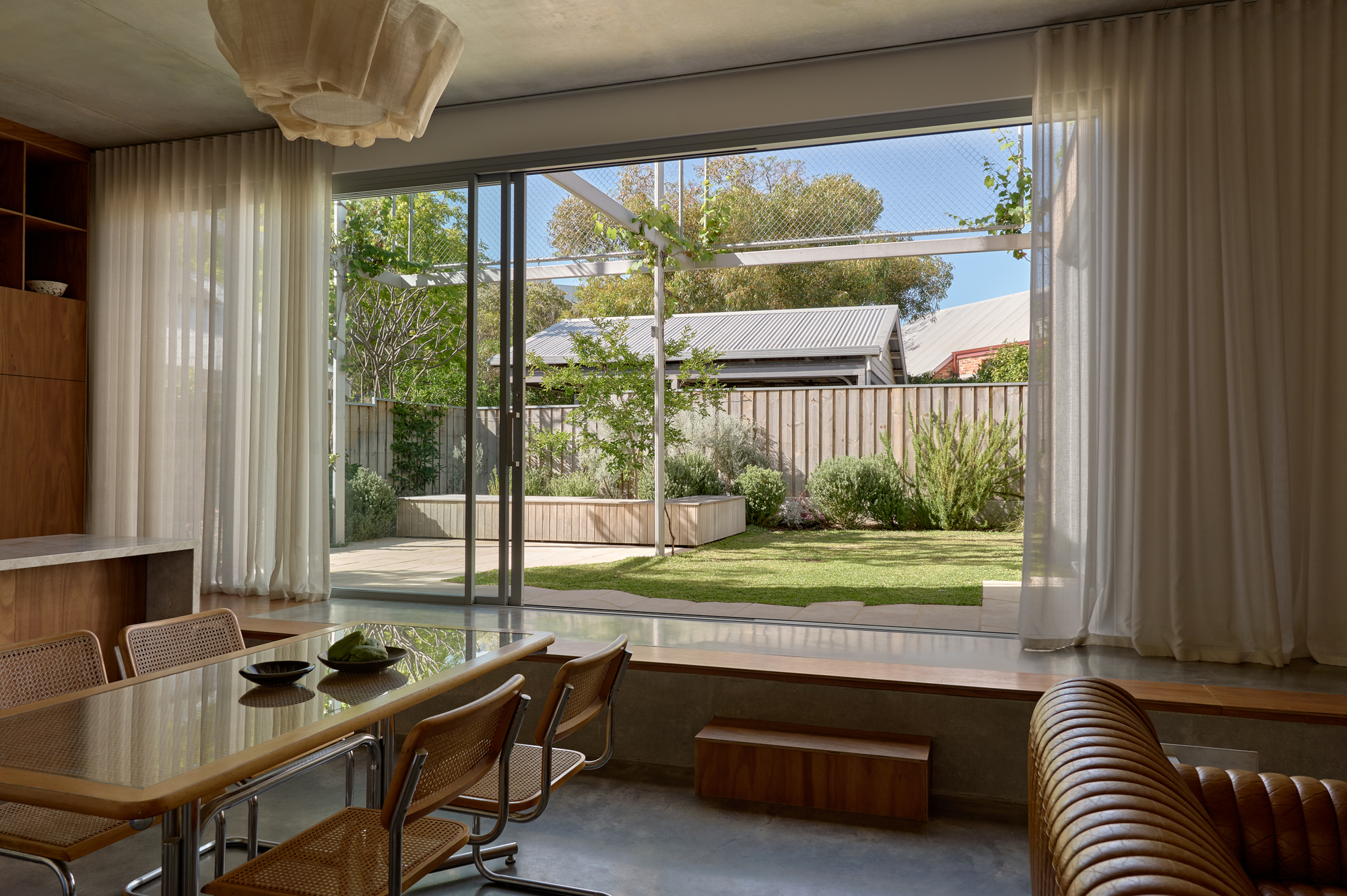 Dining area with floor-to-ceiling glazing framing a view of the planted rear garden and timber fence