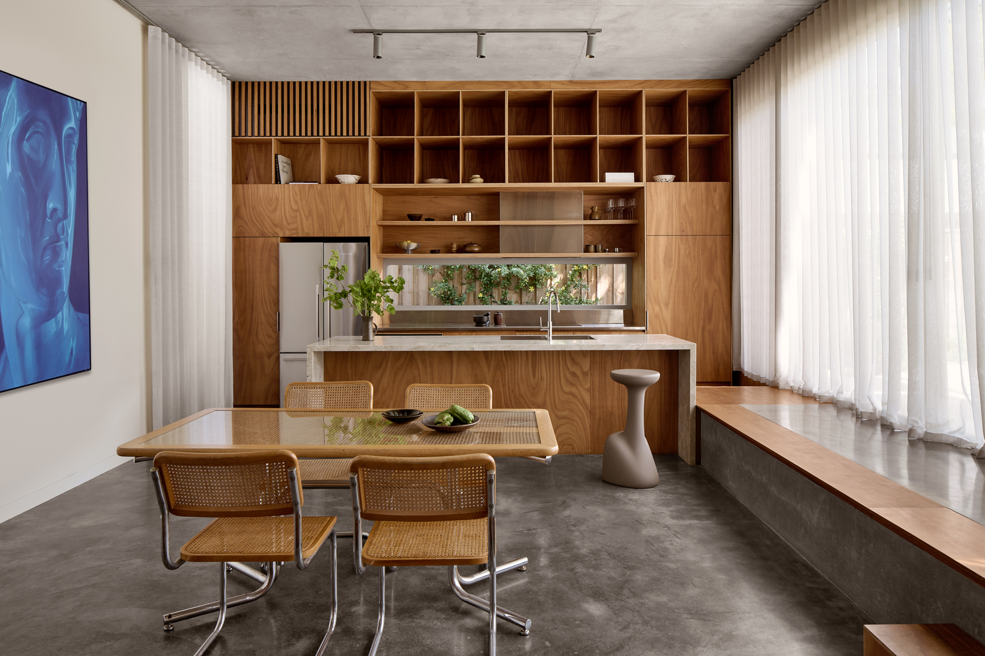 Open-plan kitchen and dining area with timber cabinetry, concrete floor, and floor-to-ceiling sheer curtains