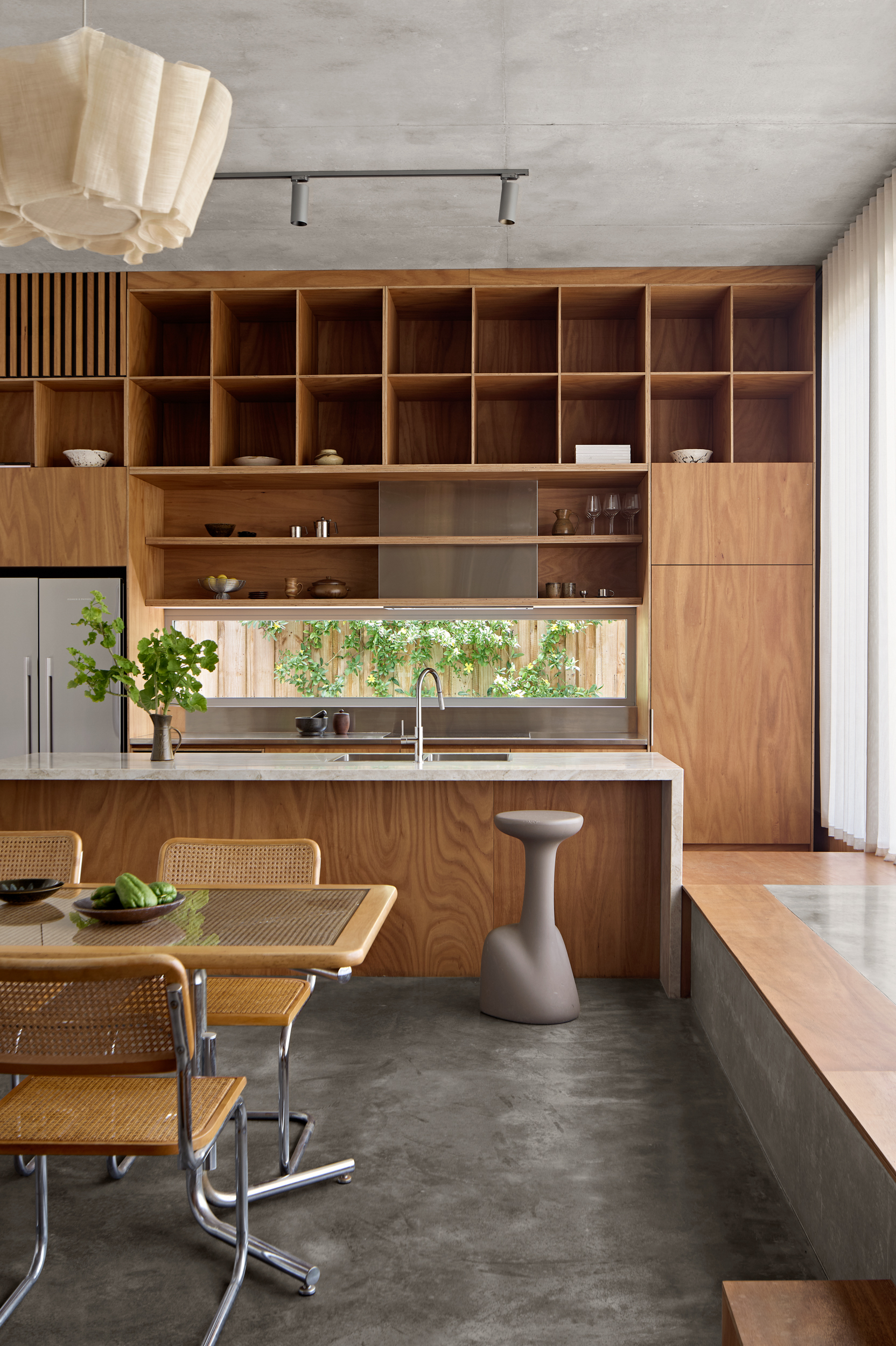 Kitchen wall with gridded timber shelving above horizontal window strip framing planted courtyard beyond