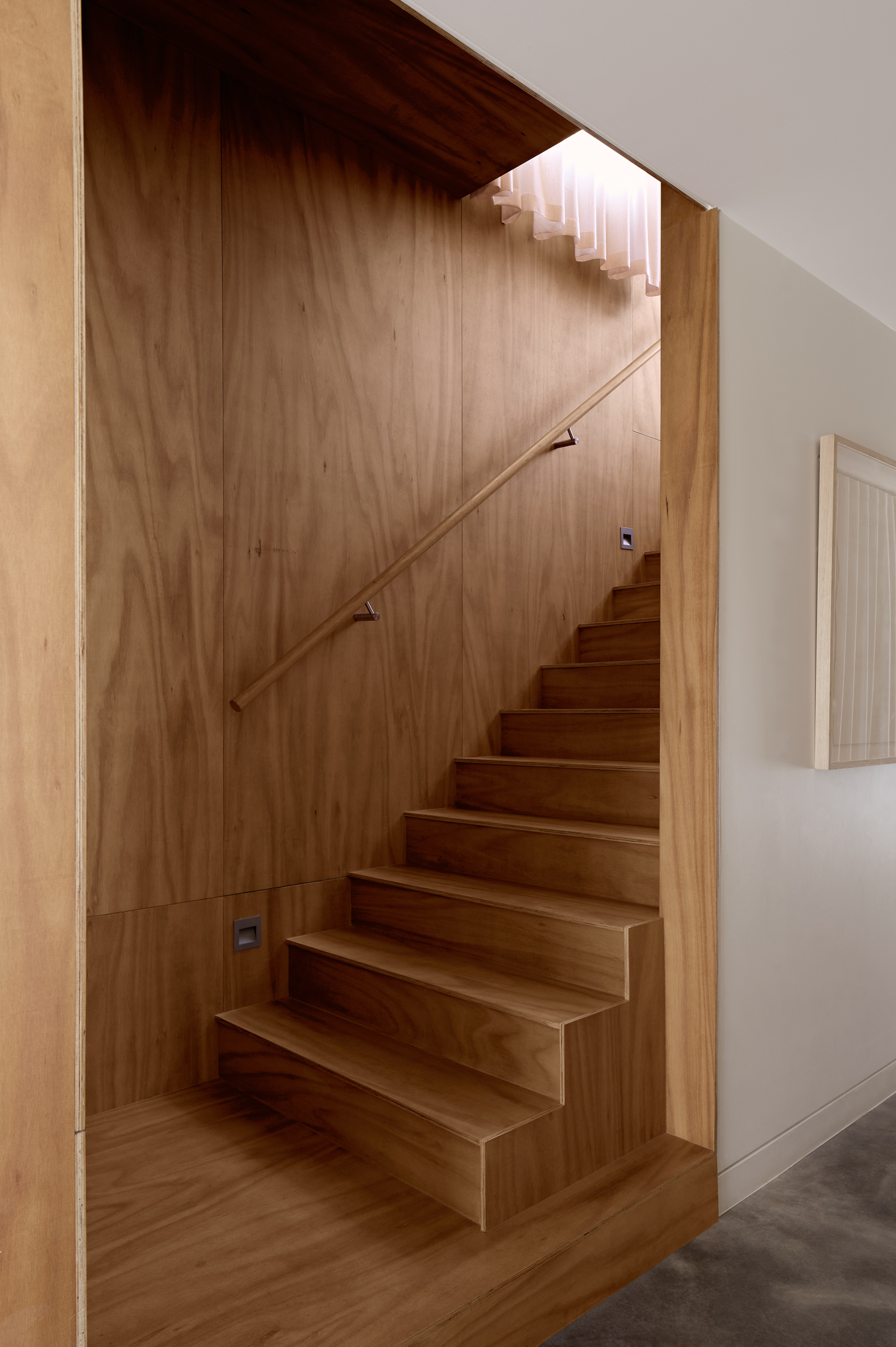 Timber-clad staircase with integrated handrail and skylight above the landing