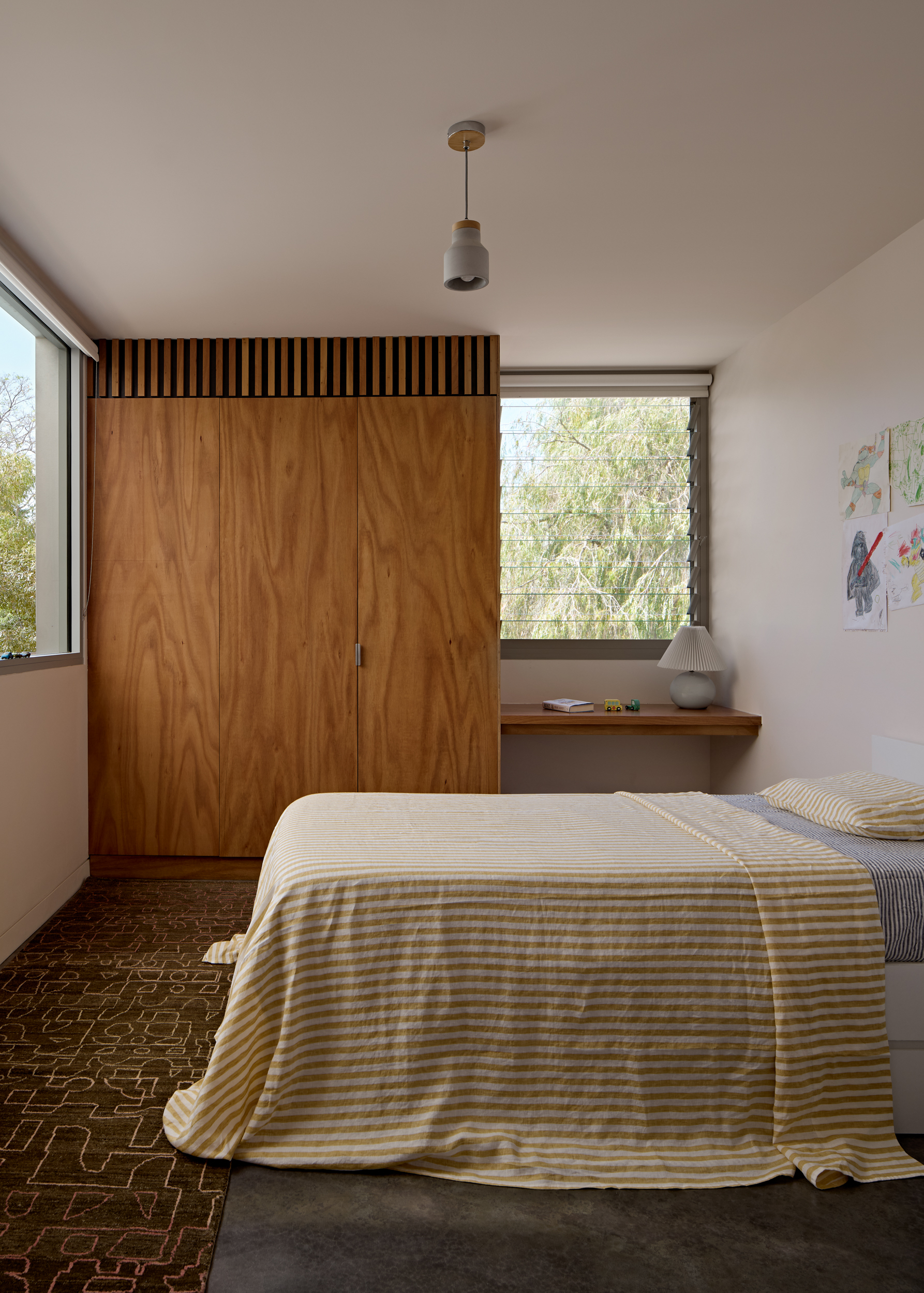 Bedroom with timber wardrobe, slatted detail above, and corner windows framing trees outside