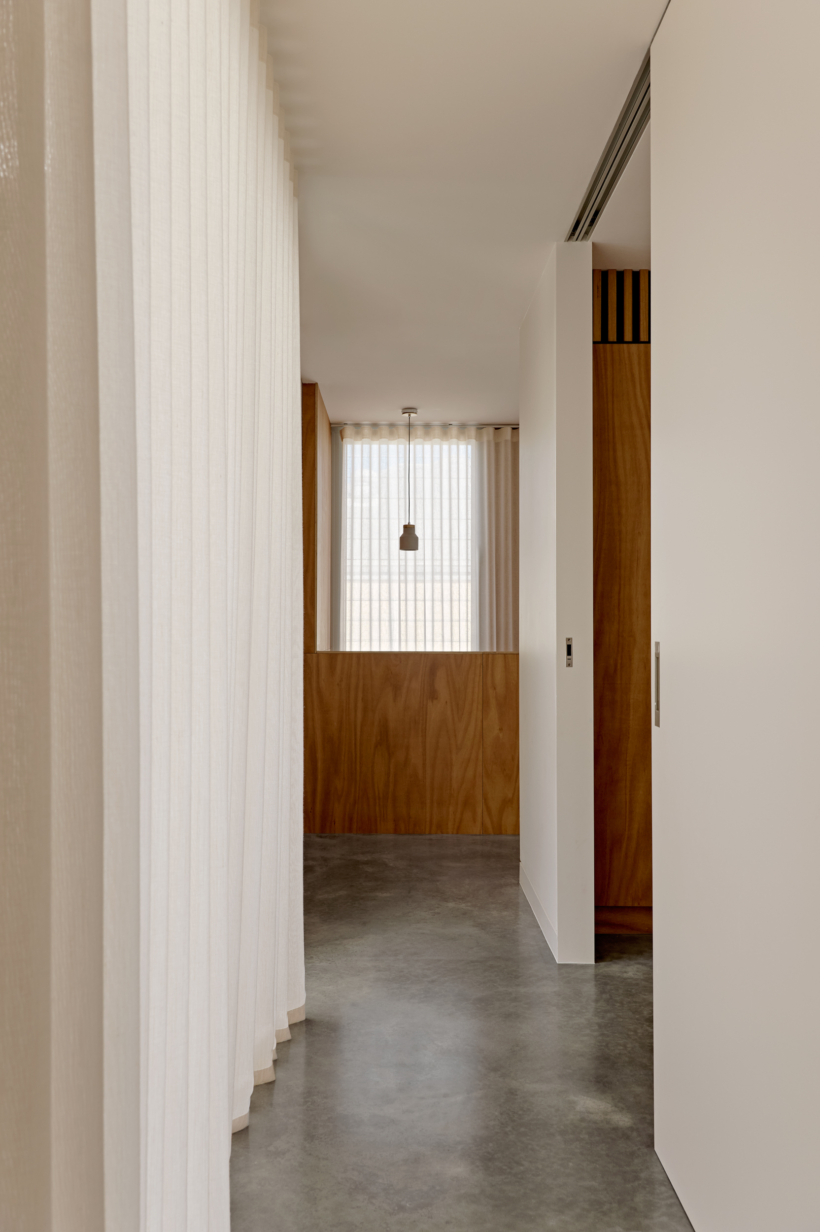 Hallway with polished concrete floor, white ribbed curtain and timber-clad partition under diffused daylight