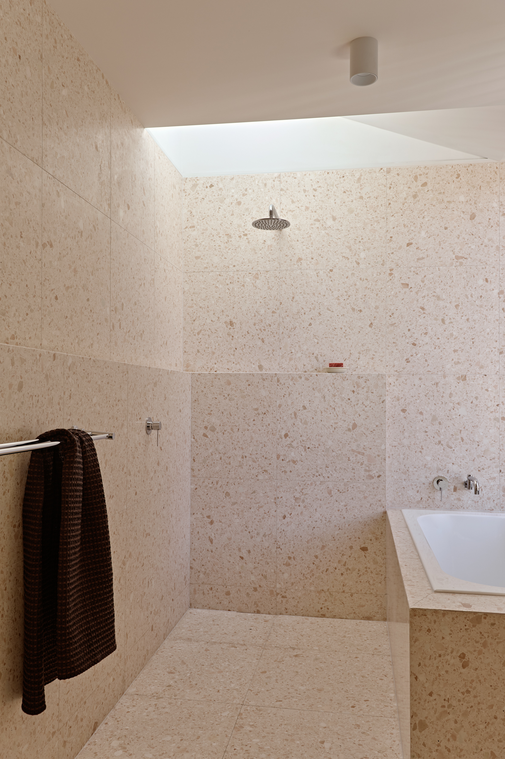Terrazzo-clad bathroom with recessed skylight above walk-in shower and wall-mounted rain head