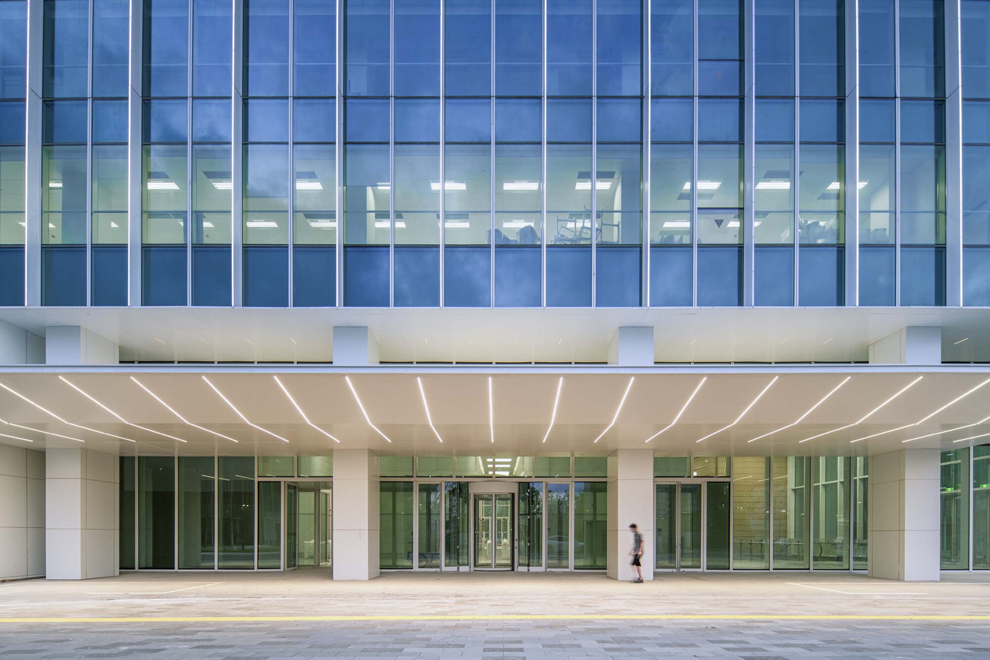 Ground-level entrance with white columns, curved canopy soffit, and curtain wall above as a figure walks past
