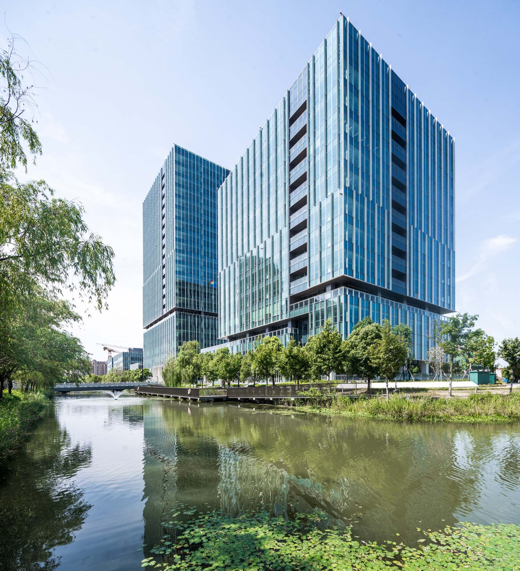 View across a pond with lily pads toward vertical glass and metal-clad towers
