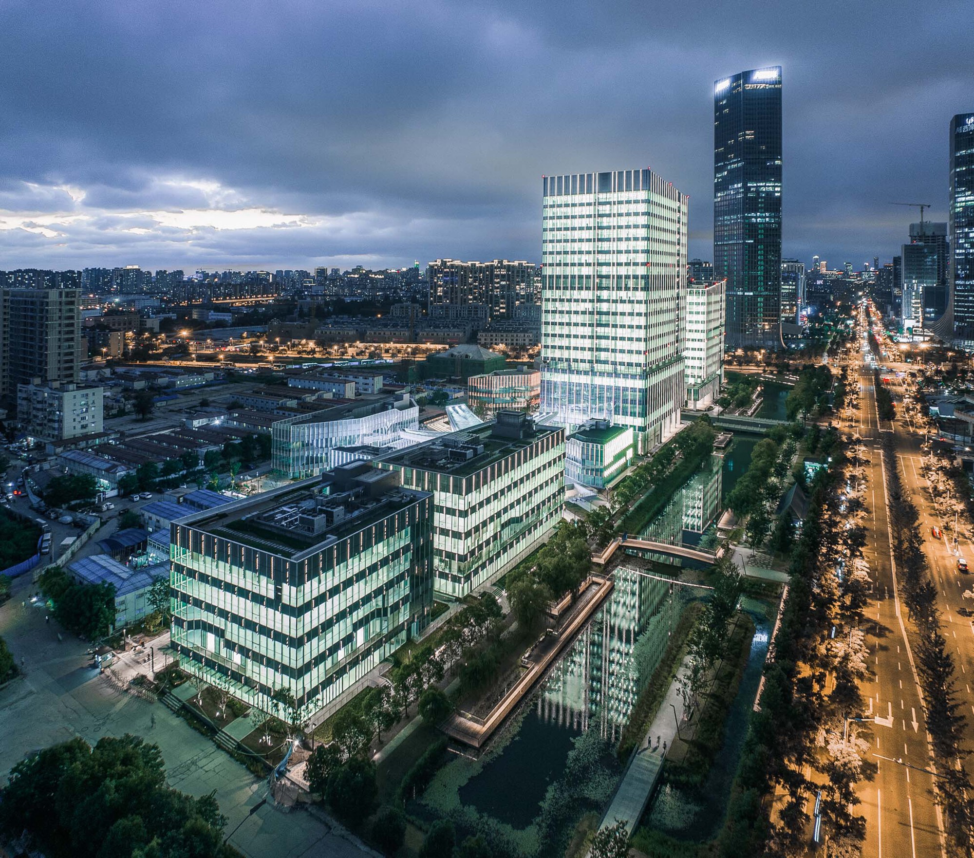 Elevated view of illuminated mixed-use towers along a tree-lined boulevard at twilight
