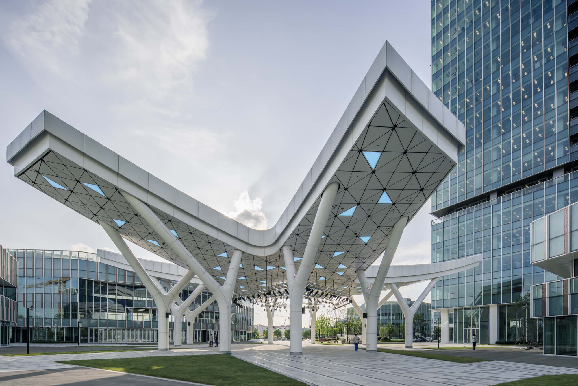Elevated canopy with triangulated soffit and white branching columns spanning between glass towers