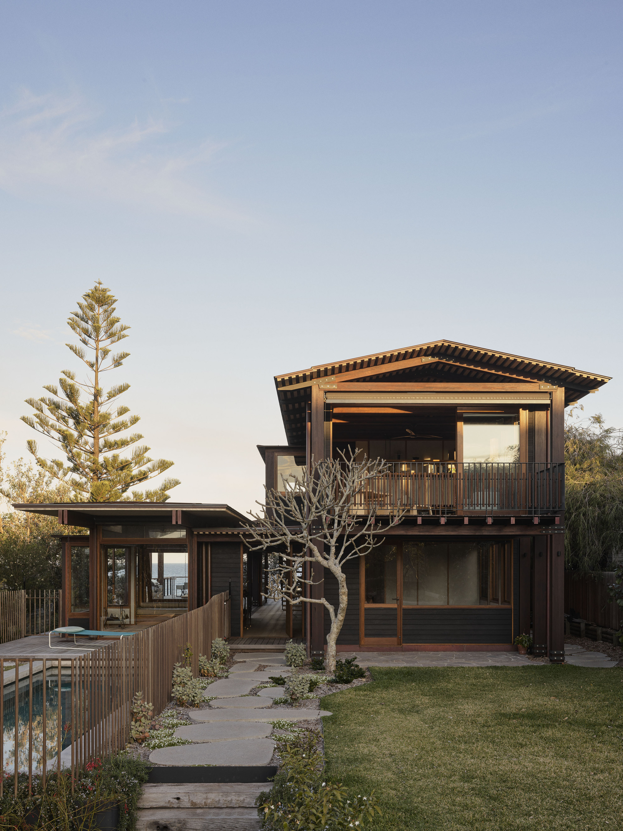 Garden view of timber-framed volumes with deep overhangs and a bare tree in the lawn