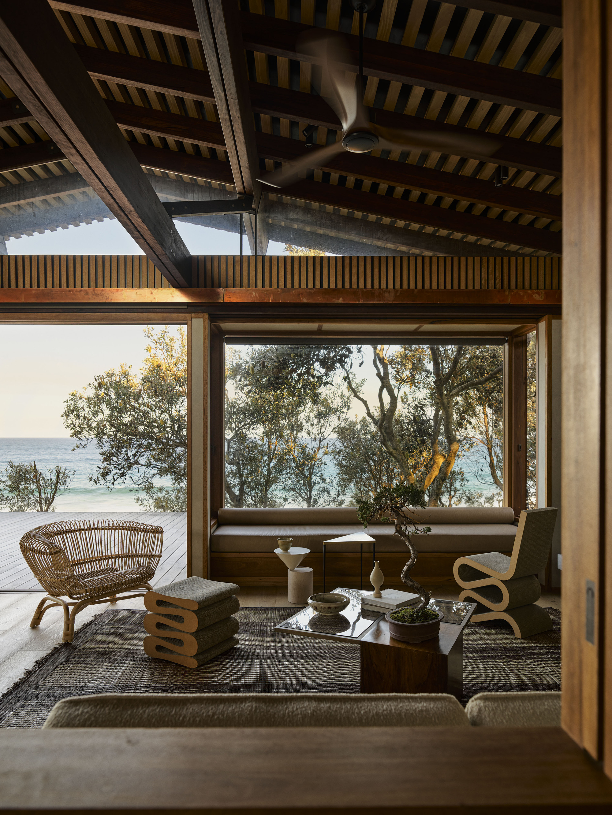 Glazed corner opening framing ocean views through coastal vegetation with slatted ceiling above