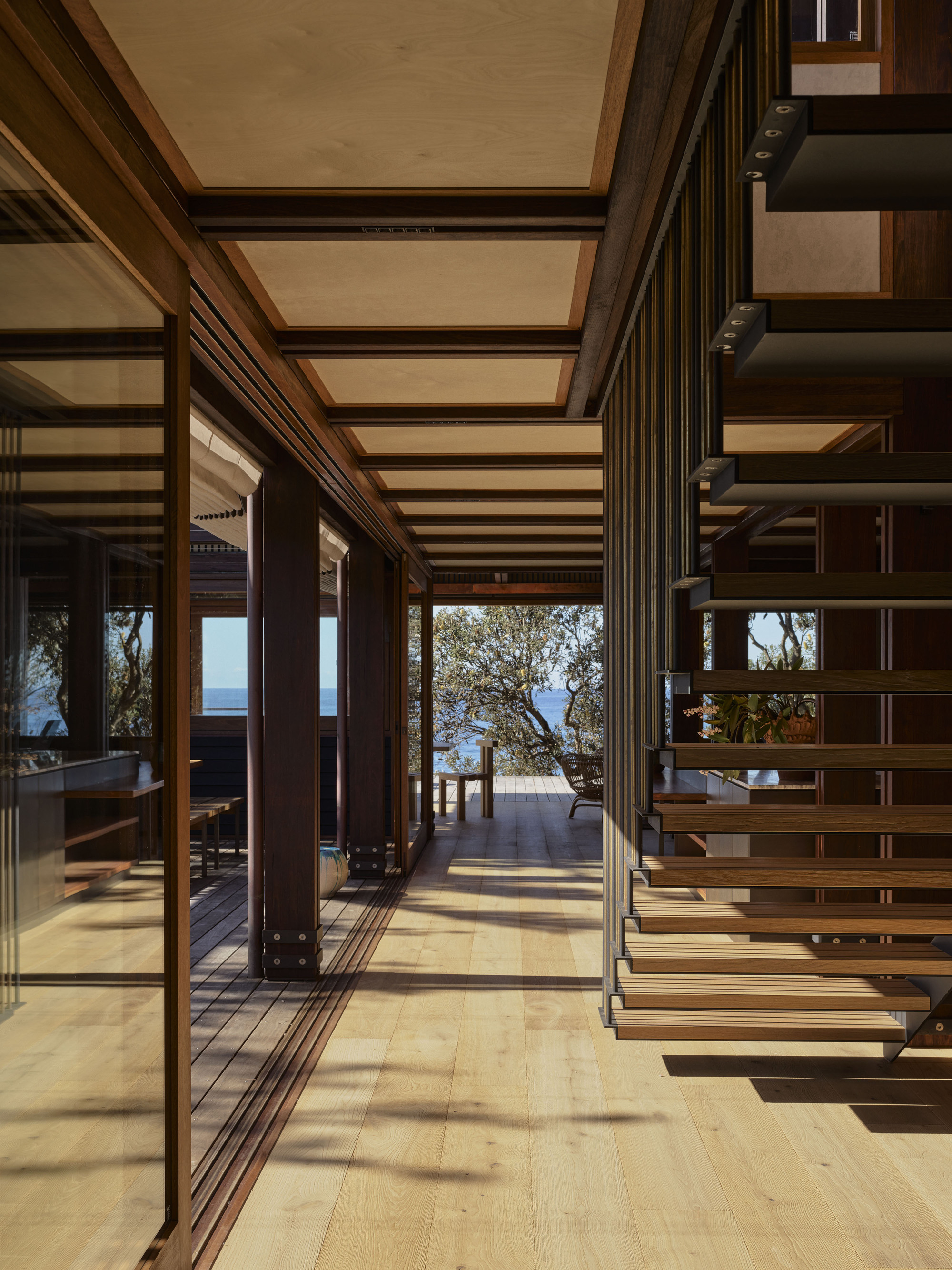 Open-tread timber stair beside folding glass doors leading to a deck with ocean horizon