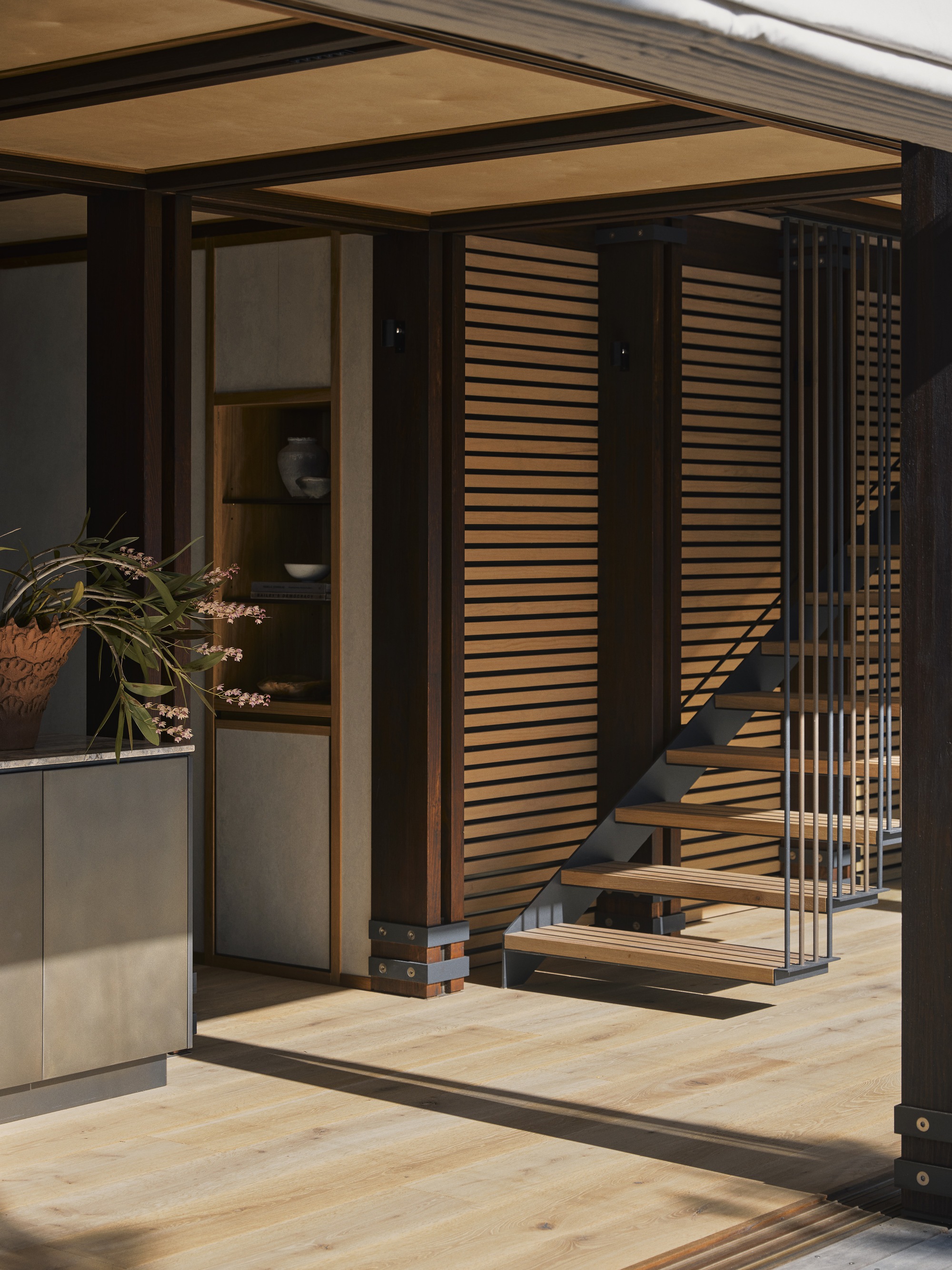 Open timber-framed threshold with horizontal slatted screens flanking a steel and wood staircase