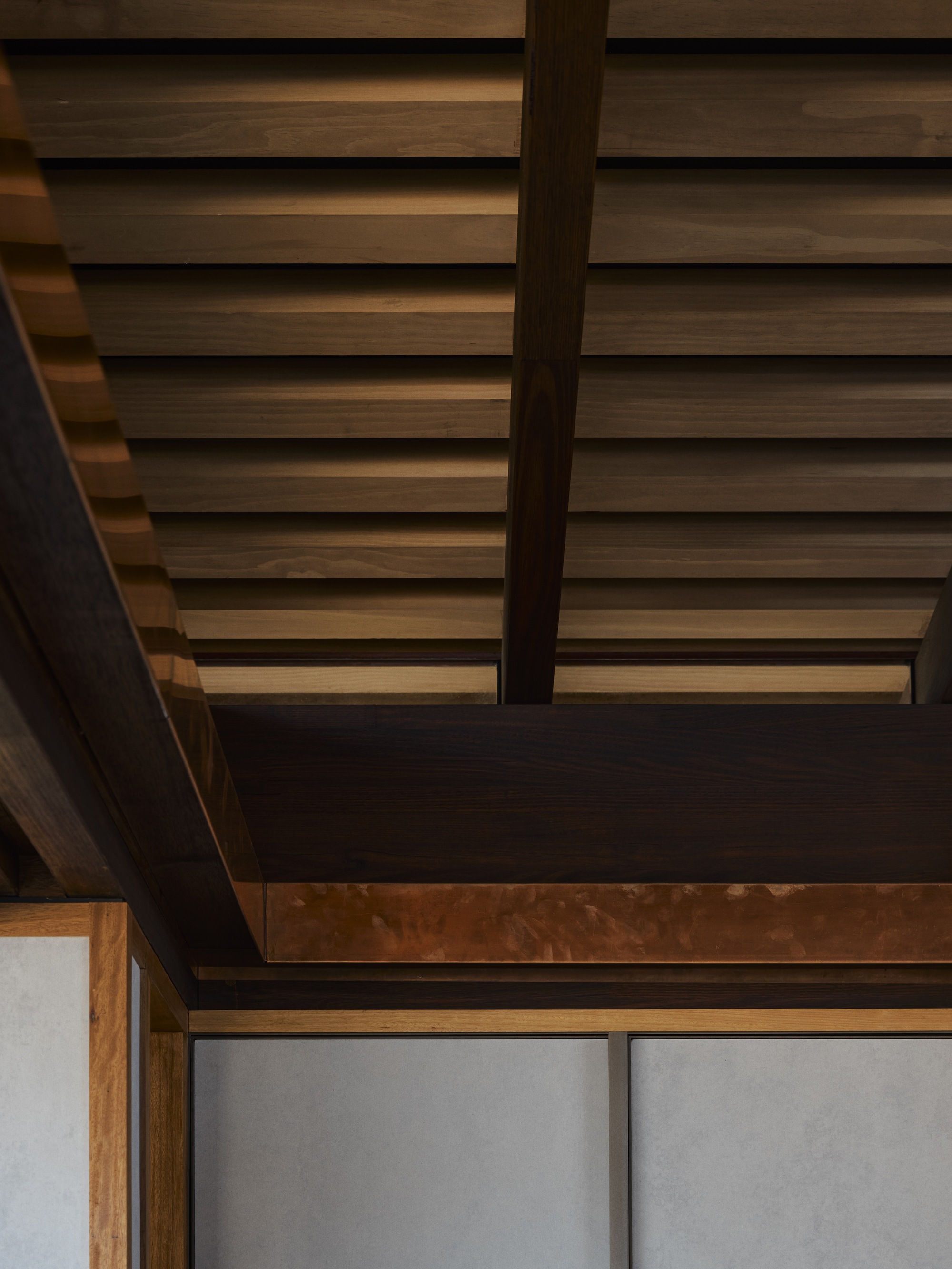 Detail of horizontal wood slat ceiling with exposed timber beams and dark steel beam junction