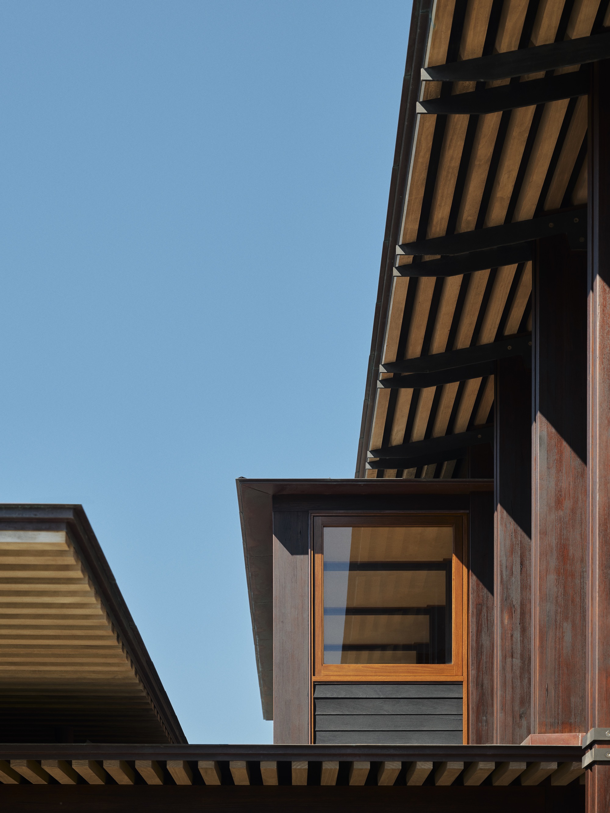 Exterior view of stacked timber volumes with slatted cladding and cantilevered roof overhang against clear sky