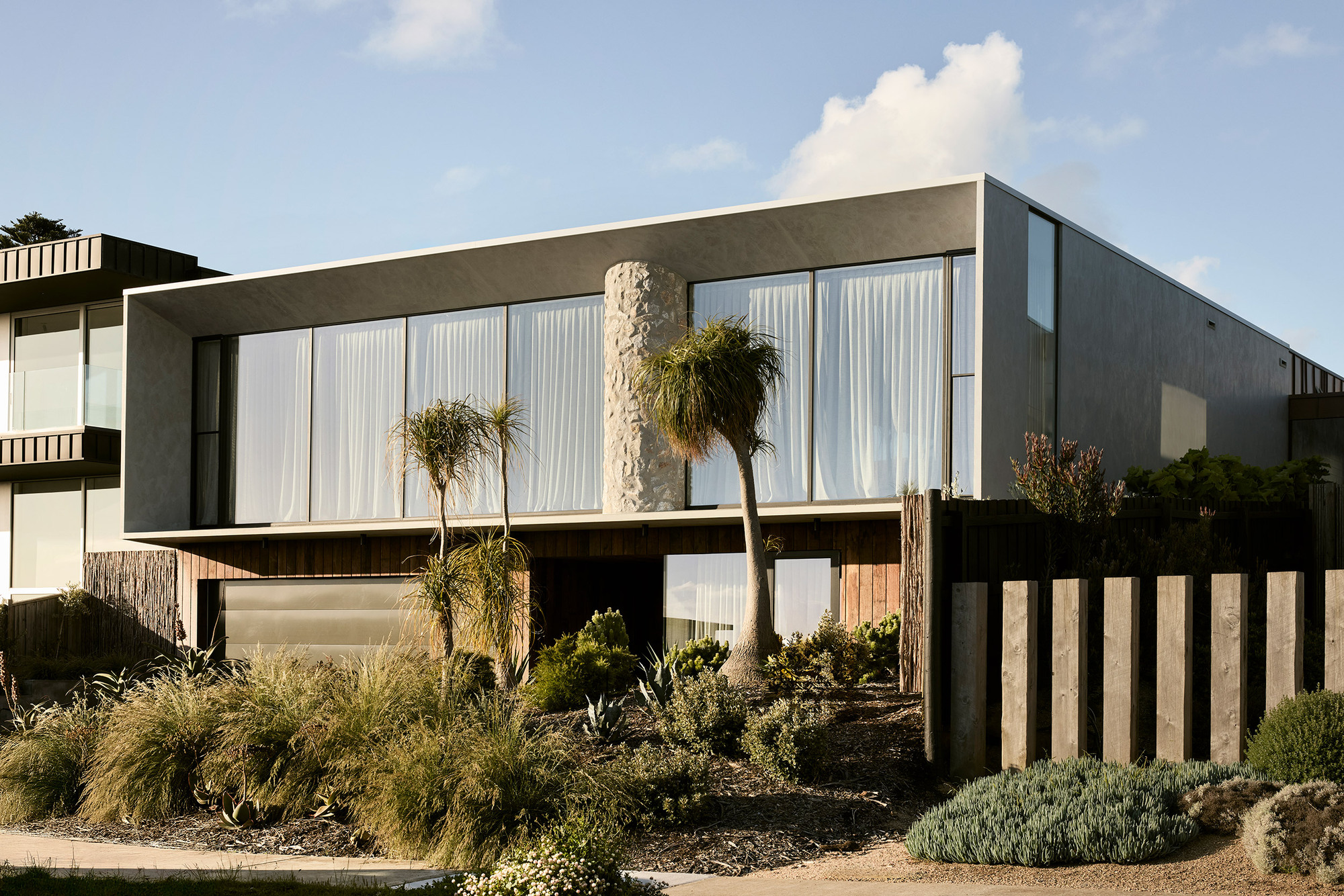 Street view of the two-story facade with white curtained glazing and planted forecourt with palms and grasses