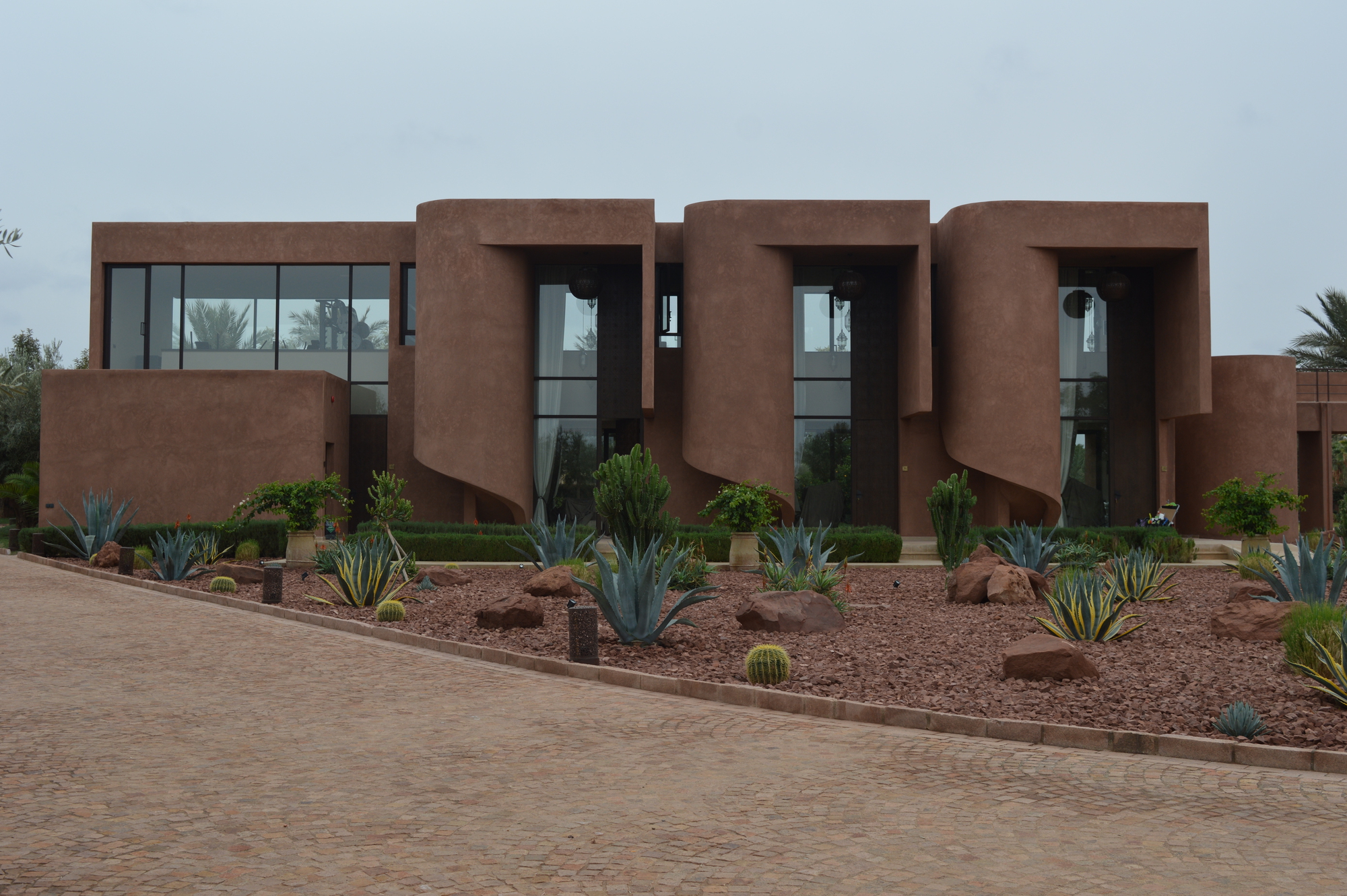 Street view of the repeating lobed facade modules with glazing and xeriscape planting below an overcast sky
