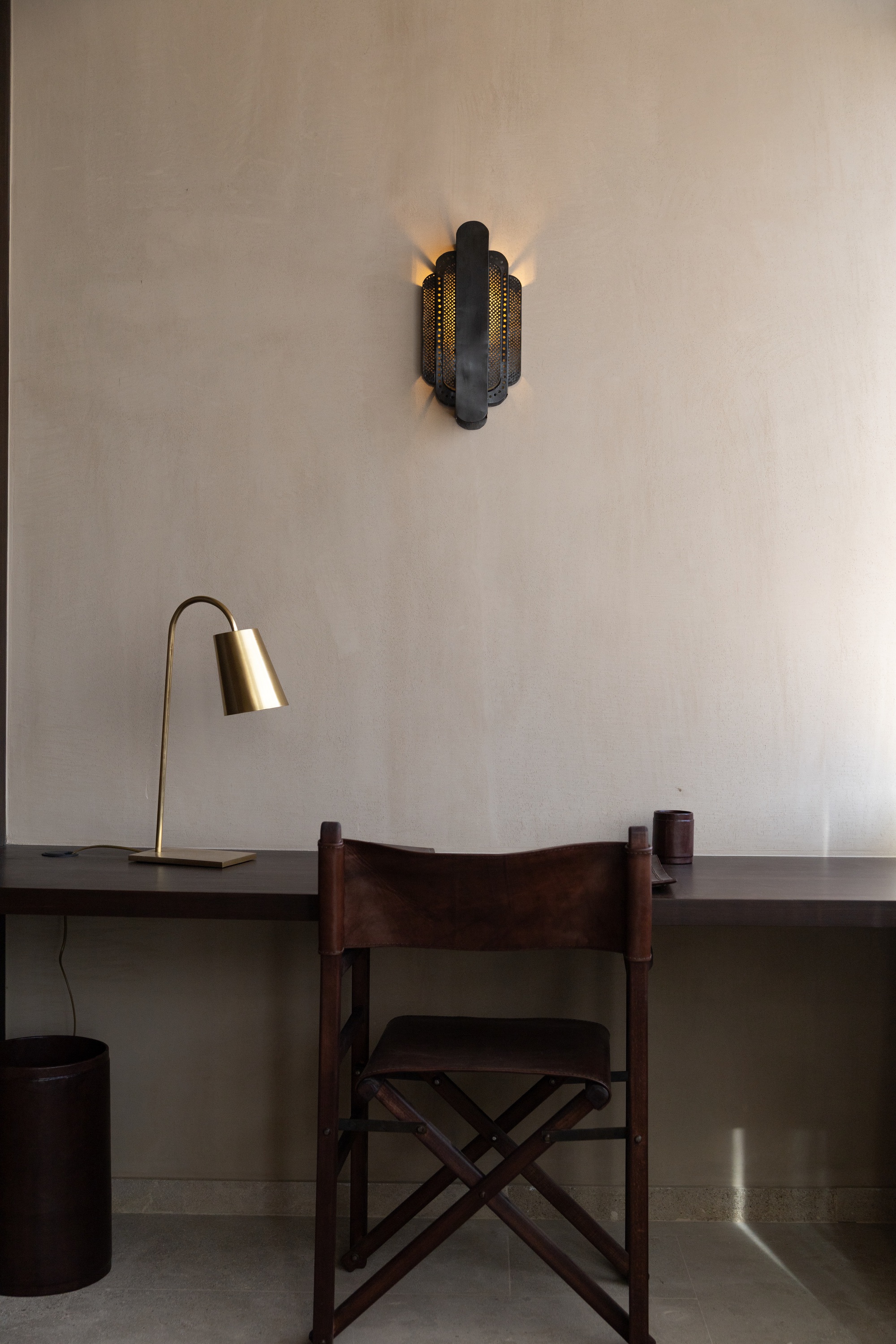 Interior workspace with timber chair, brass desk lamp and perforated metal wall sconce