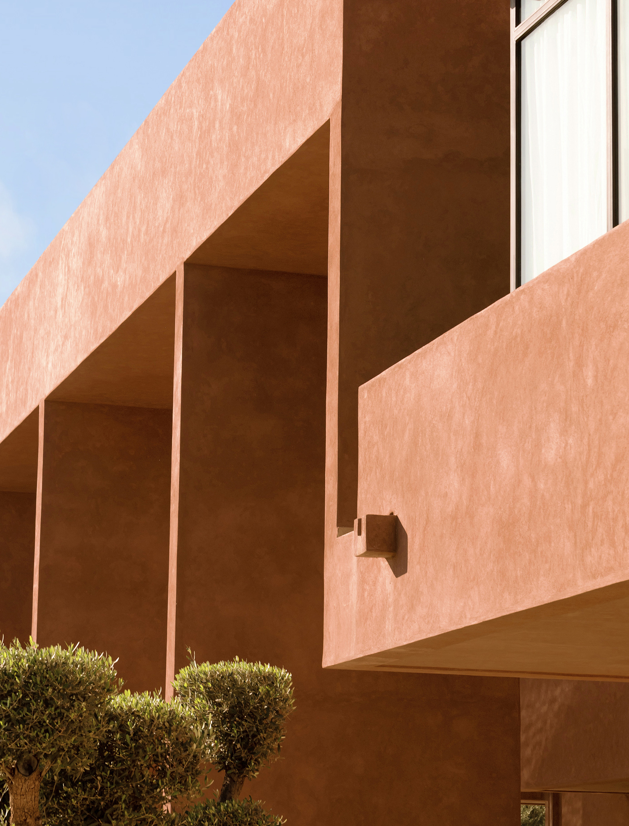 Stucco facade with deep recessed openings and slender columns framing deep shadows beneath a blue sky