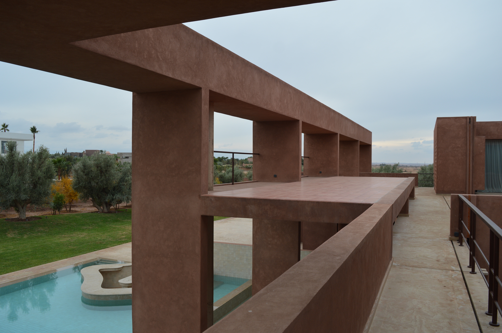 Upper-level colonnade terrace overlooking a pool and olive grove at dusk